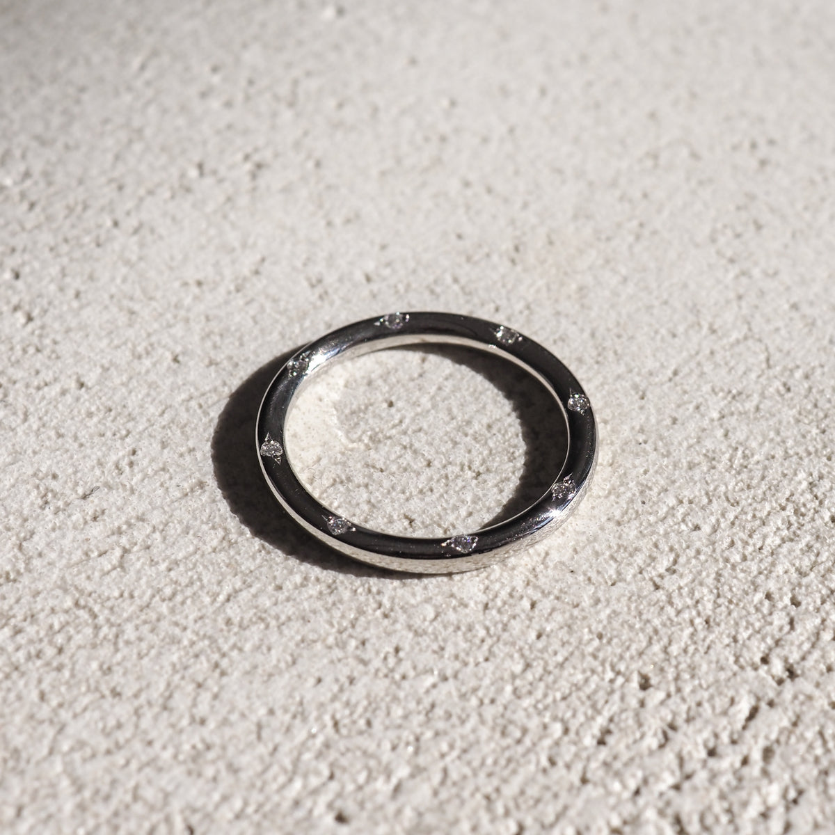 Sleek silver ring with embedded diamonds, resting on a textured light surface. High-end luxury jewellery, minimalist design.
