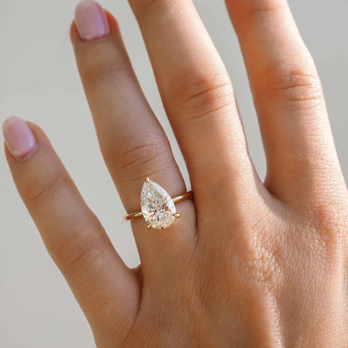 Close-up of a hand with manicured nails wearing a pear-cut diamond ring set in a gold band, showcasing luxury fine jewellery.