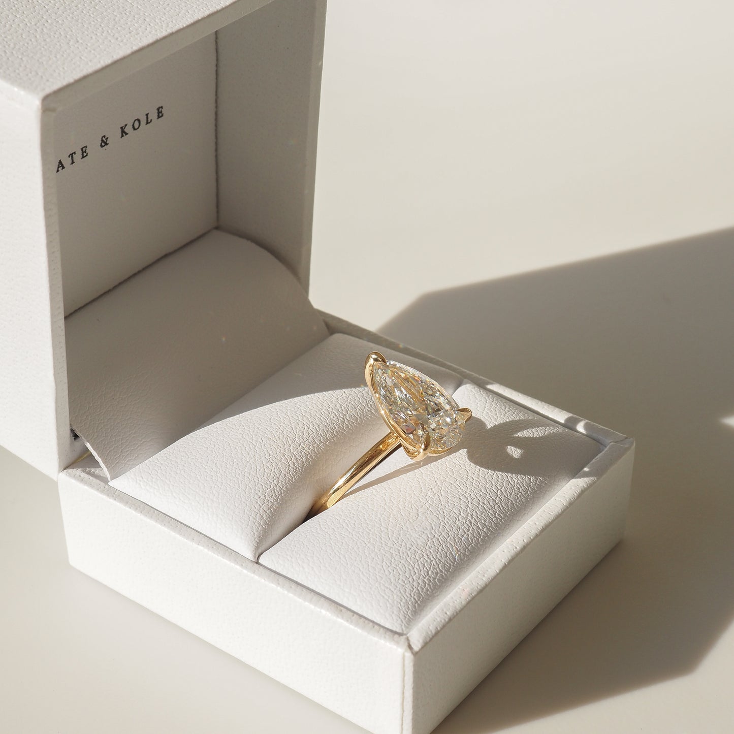 Gold marquise diamond engagement ring in a white jewellery box, catching light elegantly. Perfect for luxury and high-end jewellery enthusiasts.