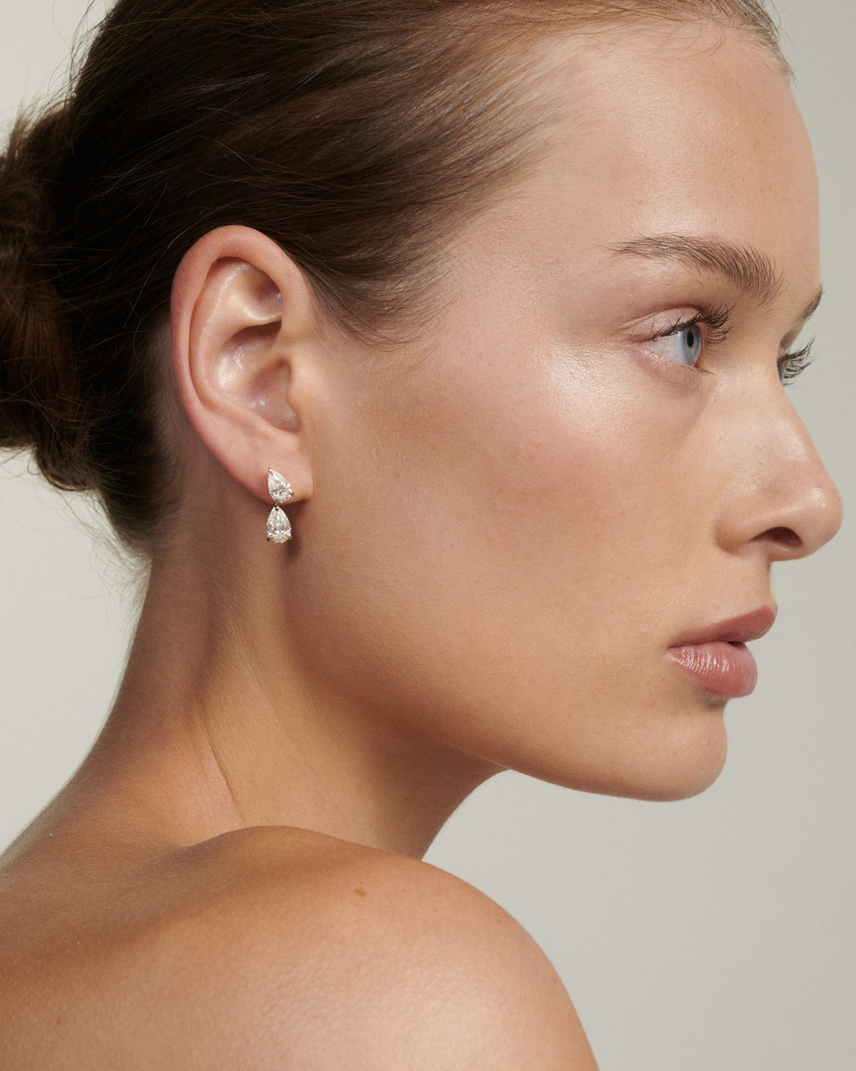 Close-up of a woman wearing pear-shaped earrings with a neutral background
