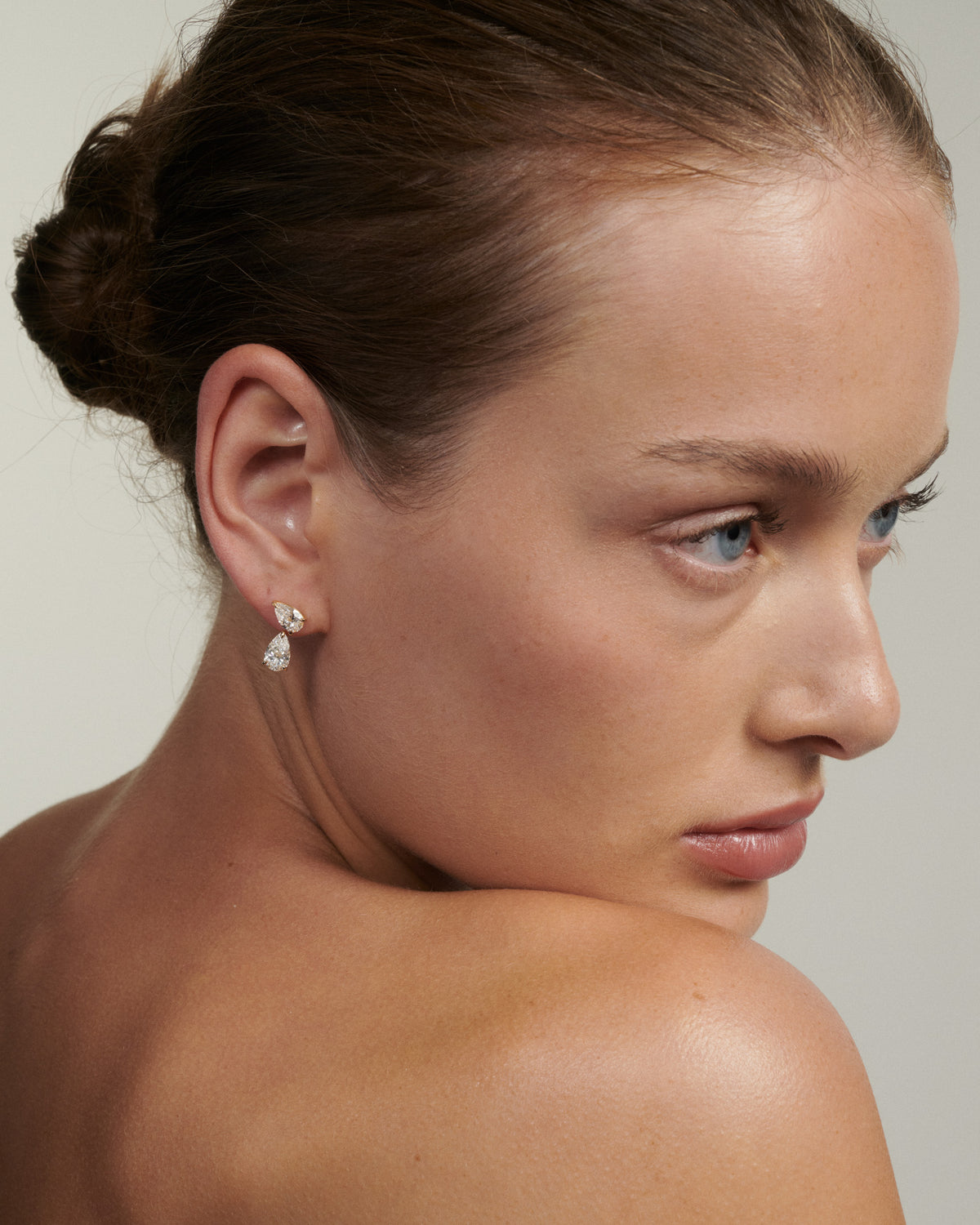 Close-up of a woman wearing diamond earrings with a neutral background