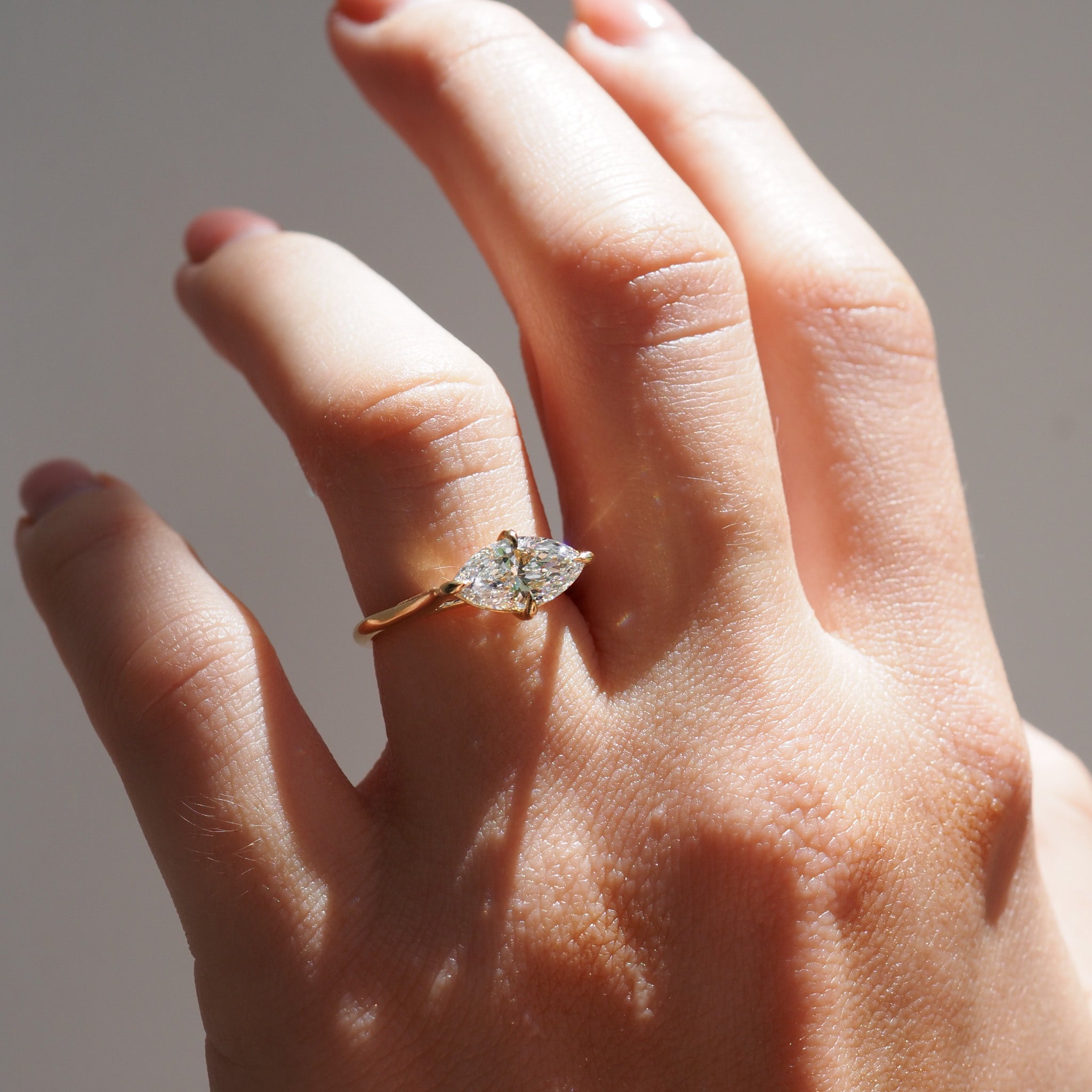 Women's hand wearing a diamond ring on a neutral background