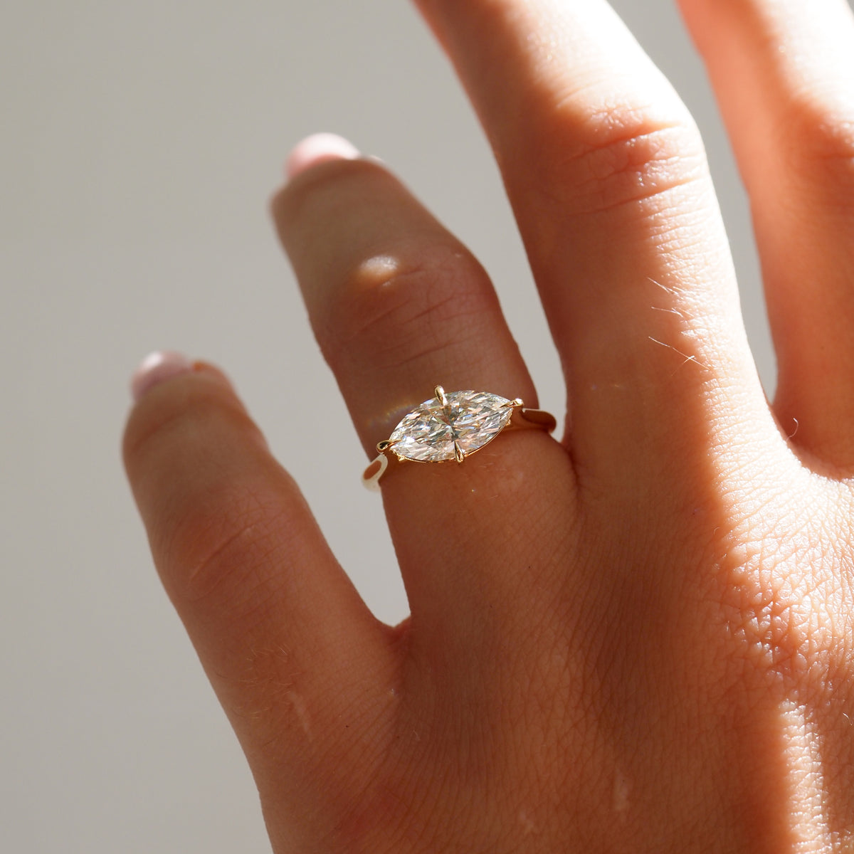 Close-up of a hand wearing a marquise diamond ring on a gold band, elegantly displayed under natural lighting.