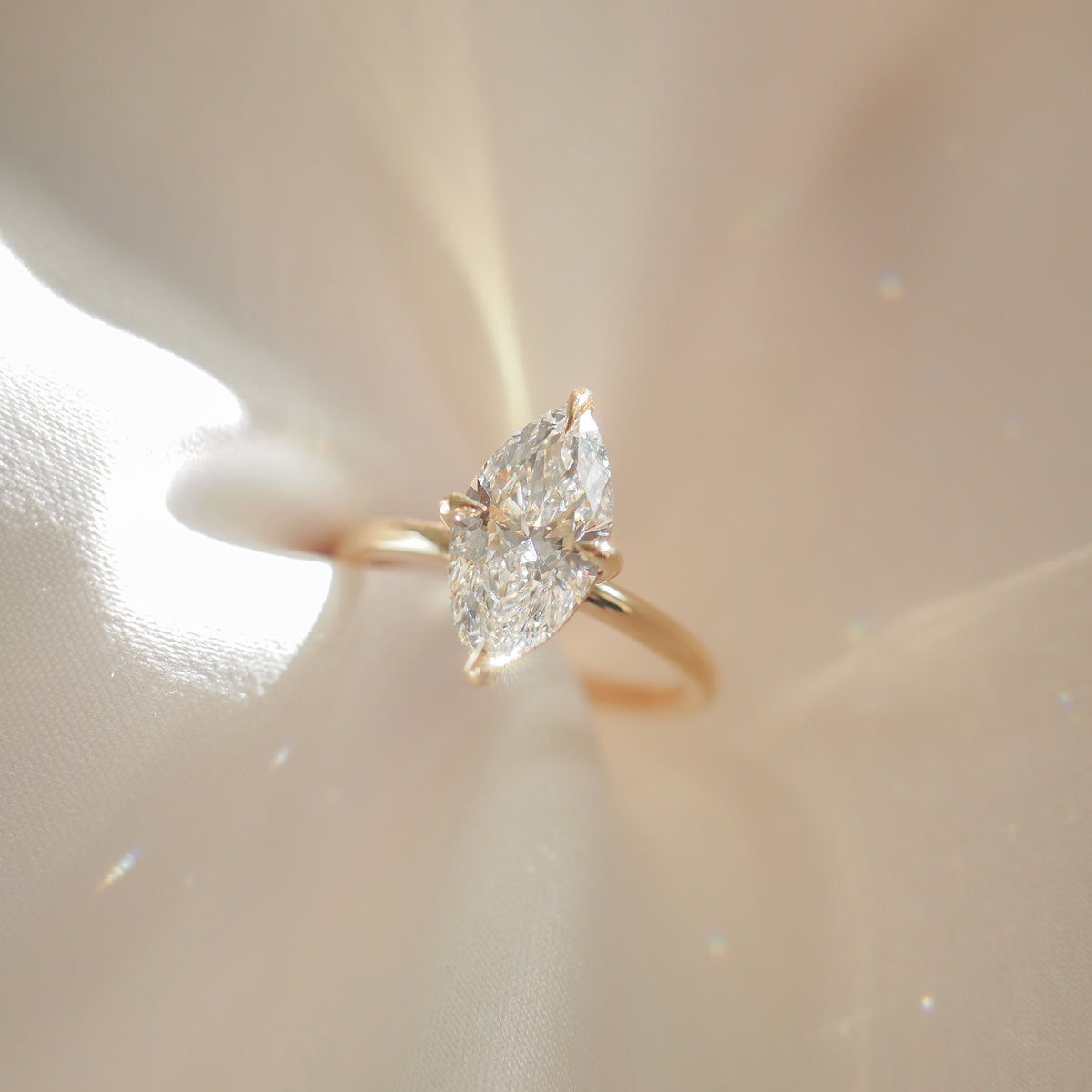 Marquise-cut diamond ring on gold band, showcased on a silky, light-reflective surface, exemplifying luxury jewellery.