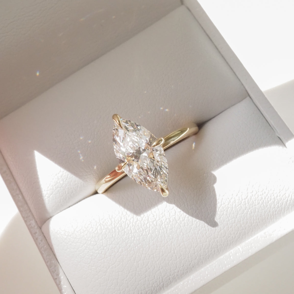 Marquise-cut diamond ring in a gold setting, showcased in an open white jewellery box, reflecting light elegantly.
