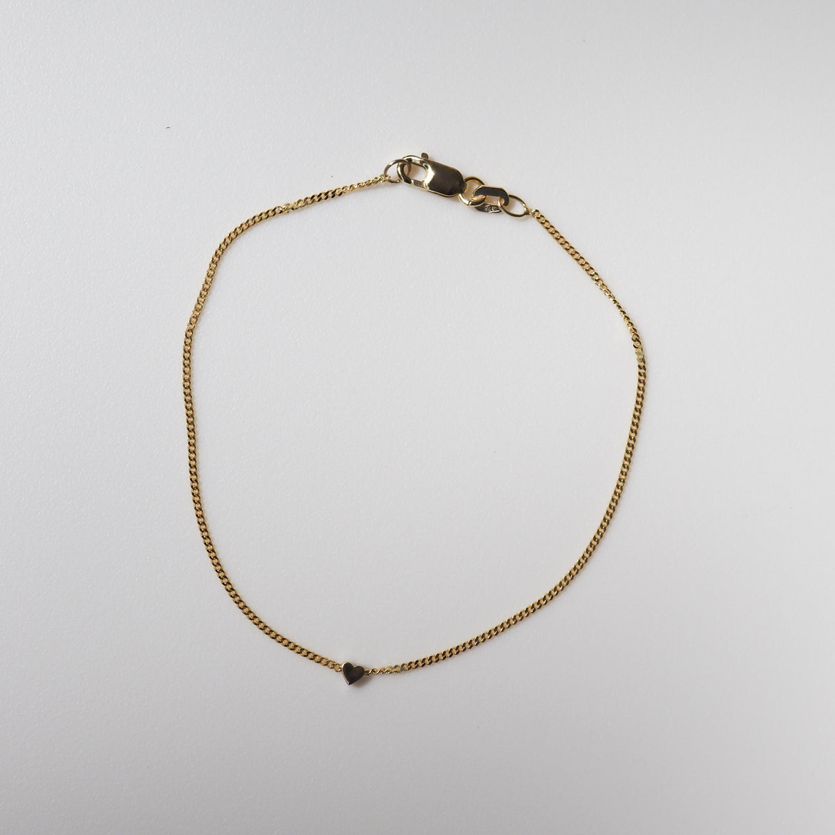 Gold chain bracelet with a heart charm on a white background, showcasing a luxurious and minimalist jewellery design.
