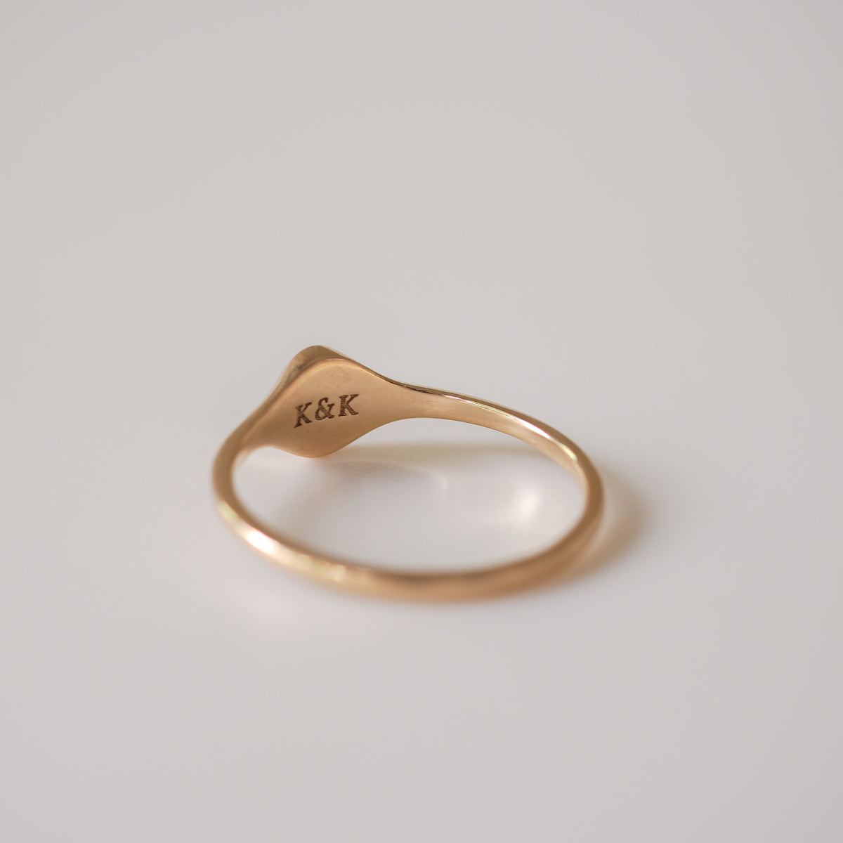 Elegant gold ring inscribed with "K&K" on a smooth, curved band against a soft white background. Luxury jewellery focus.