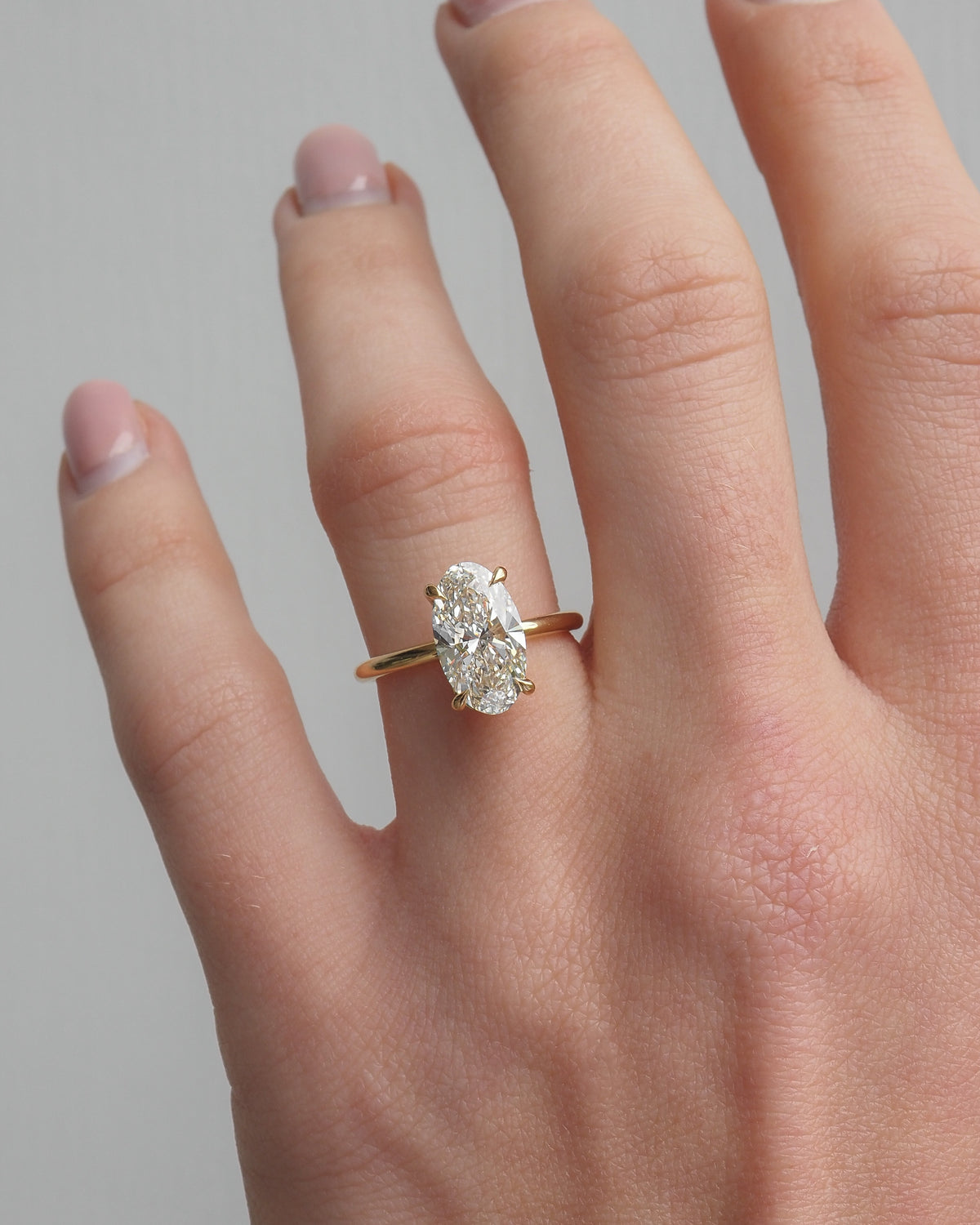 Gold oval lab-grown diamond solitaire ring on finger with oval center stone
