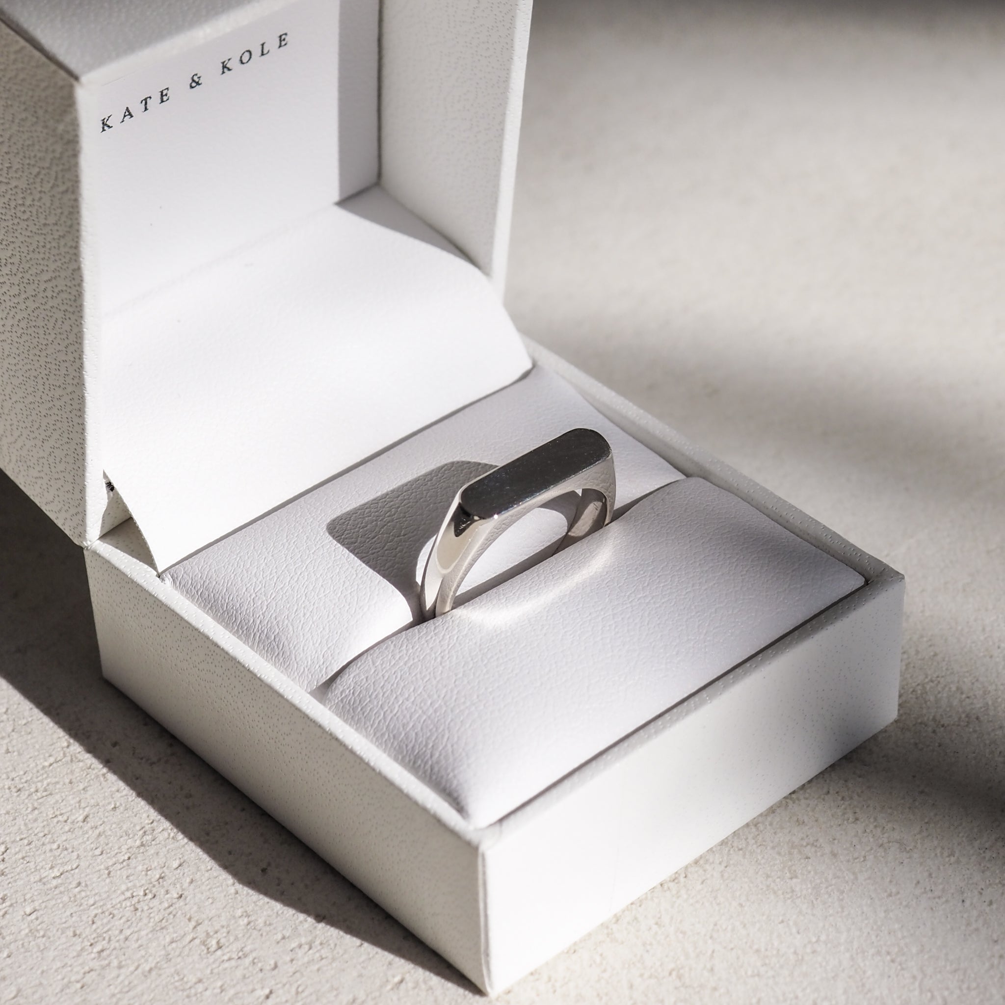 Silver ring in a white Kate & Kole jewellery box, elegantly presented on a light surface with subtle shadows.