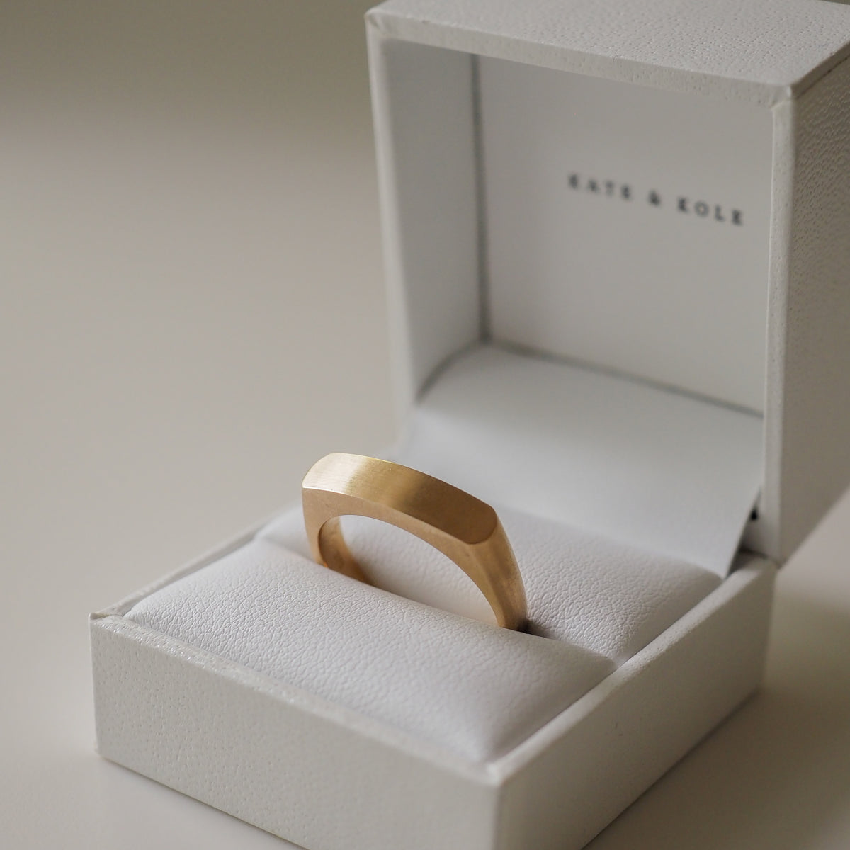 Minimalist gold ring with a flat top in a white Kate & Kole jewellery box, showcasing luxury design and craftsmanship.