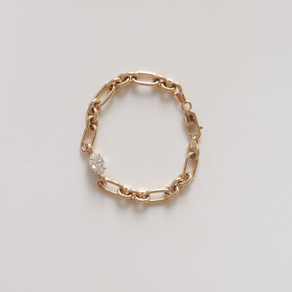 Gold chain bracelet with a cluster of sparkling diamonds on a light grey background. Luxury jewellery, elegant design, high-end style.
