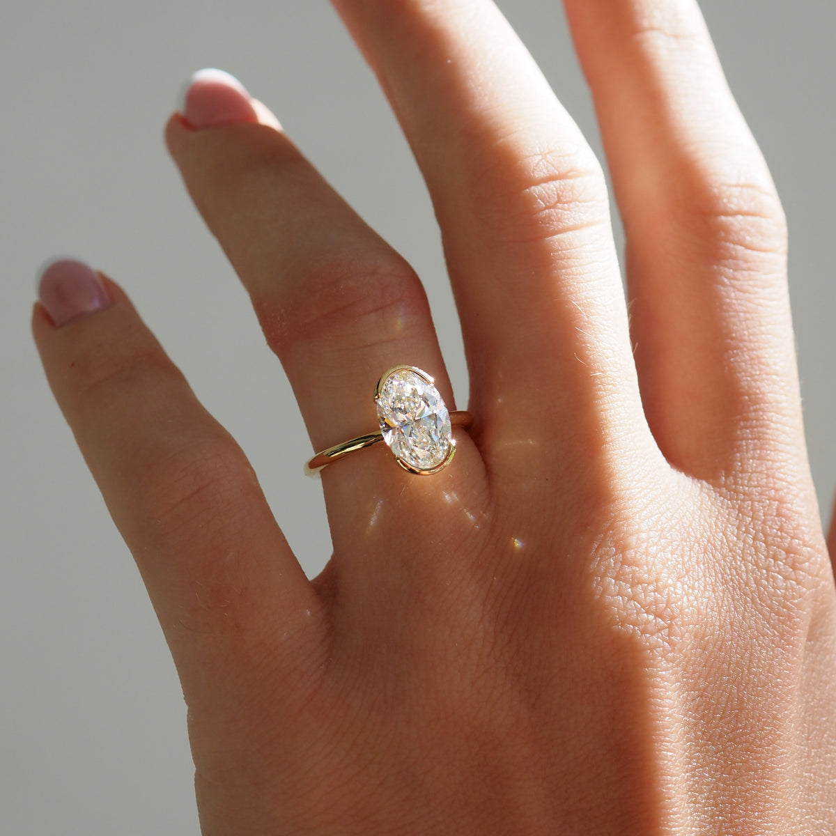 Oval gold lab-grown diamond engagement ring on hand with half bezel setting