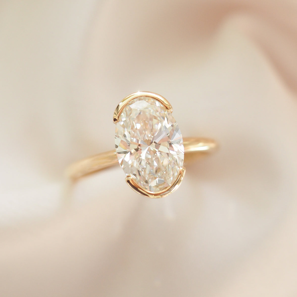 Gold oval lab-grown diamond solitaire engagement ring with half bezel setting