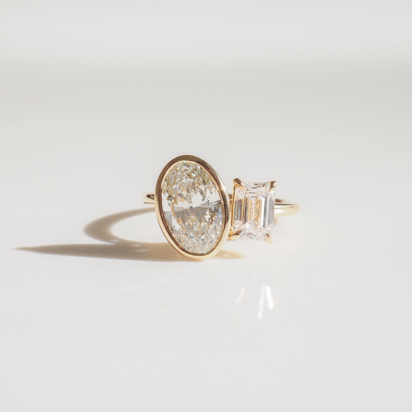 Elegant gold ring with an oval and emerald-cut diamond, set against a minimalist background, showcasing luxury design and craftsmanship.