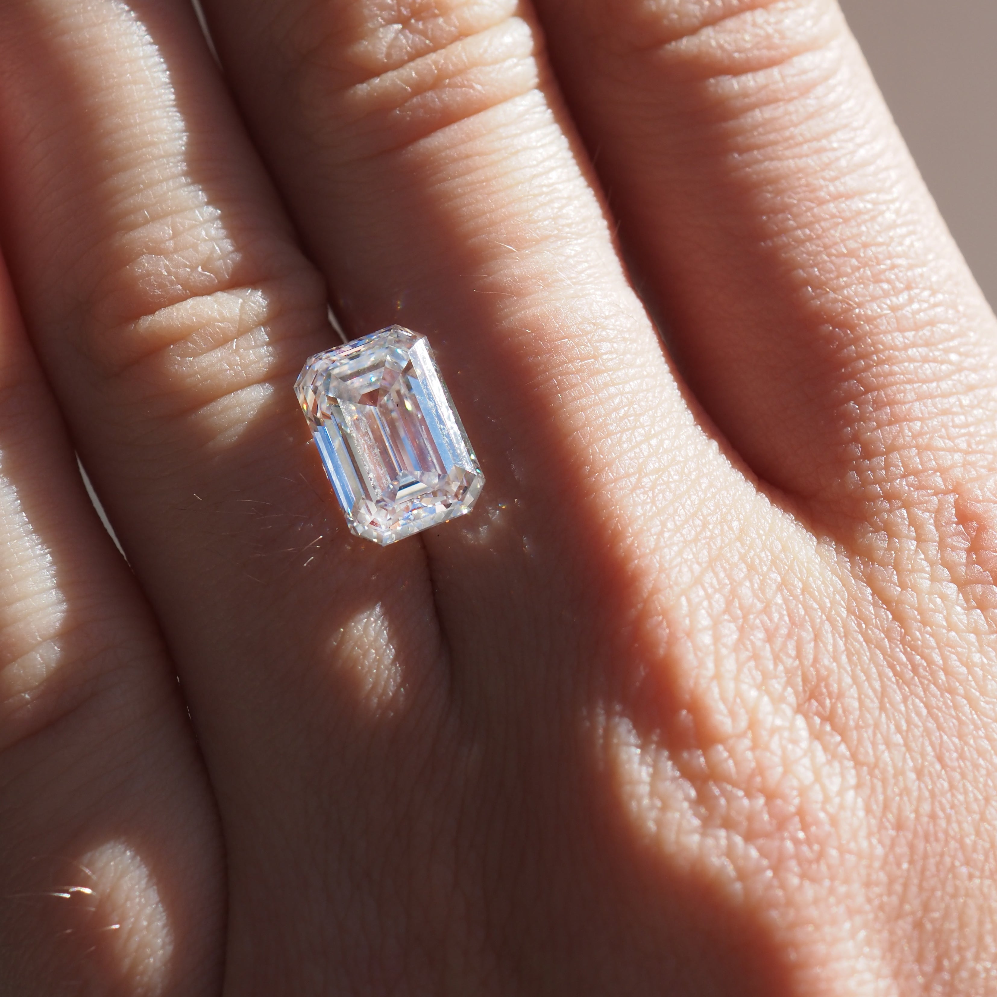 Close-up of an emerald-cut diamond ring on a finger, sparkling in natural light, showcasing luxury jewellery craftsmanship.