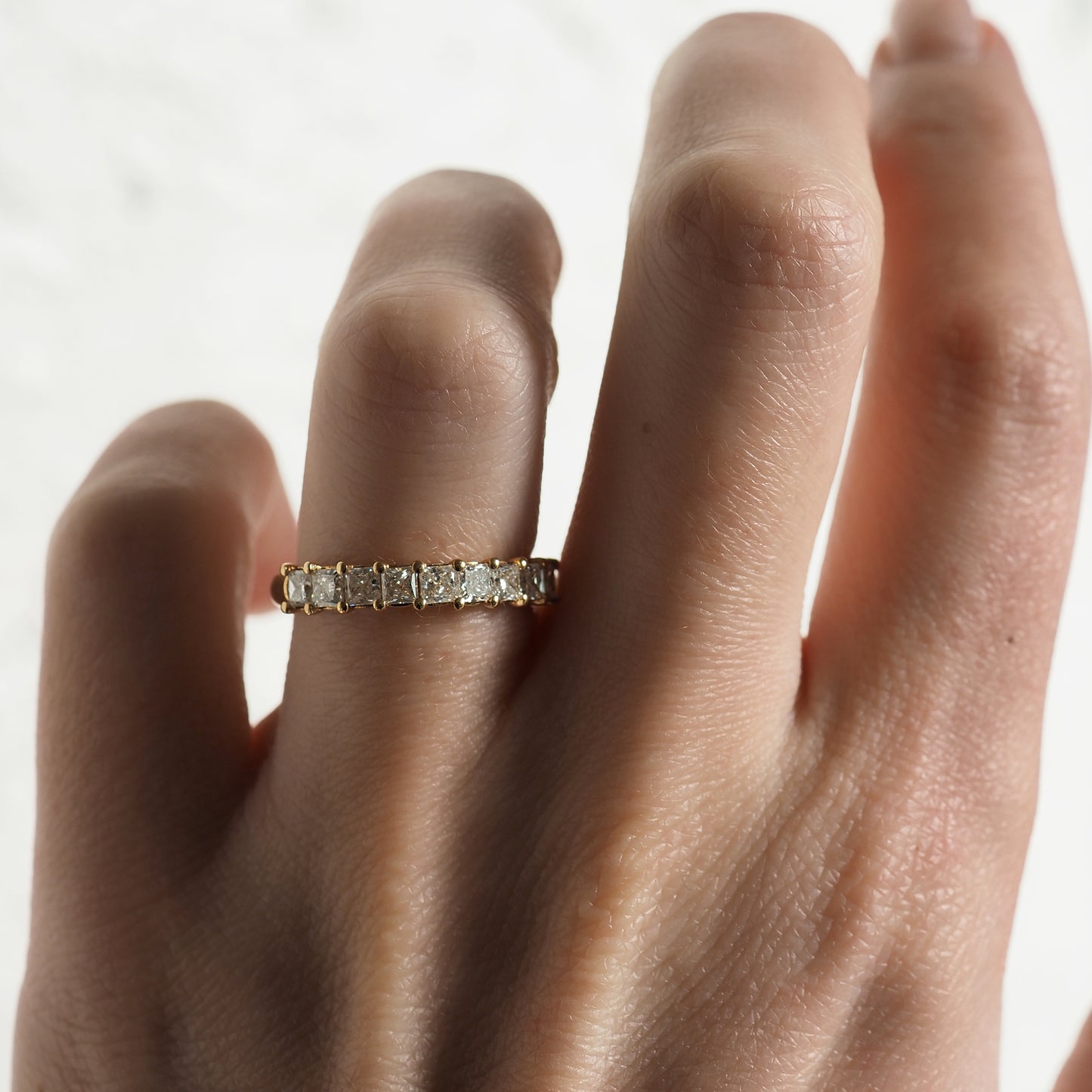 Hand wearing a luxury gold ring adorned with sparkling square diamonds on a light background.
