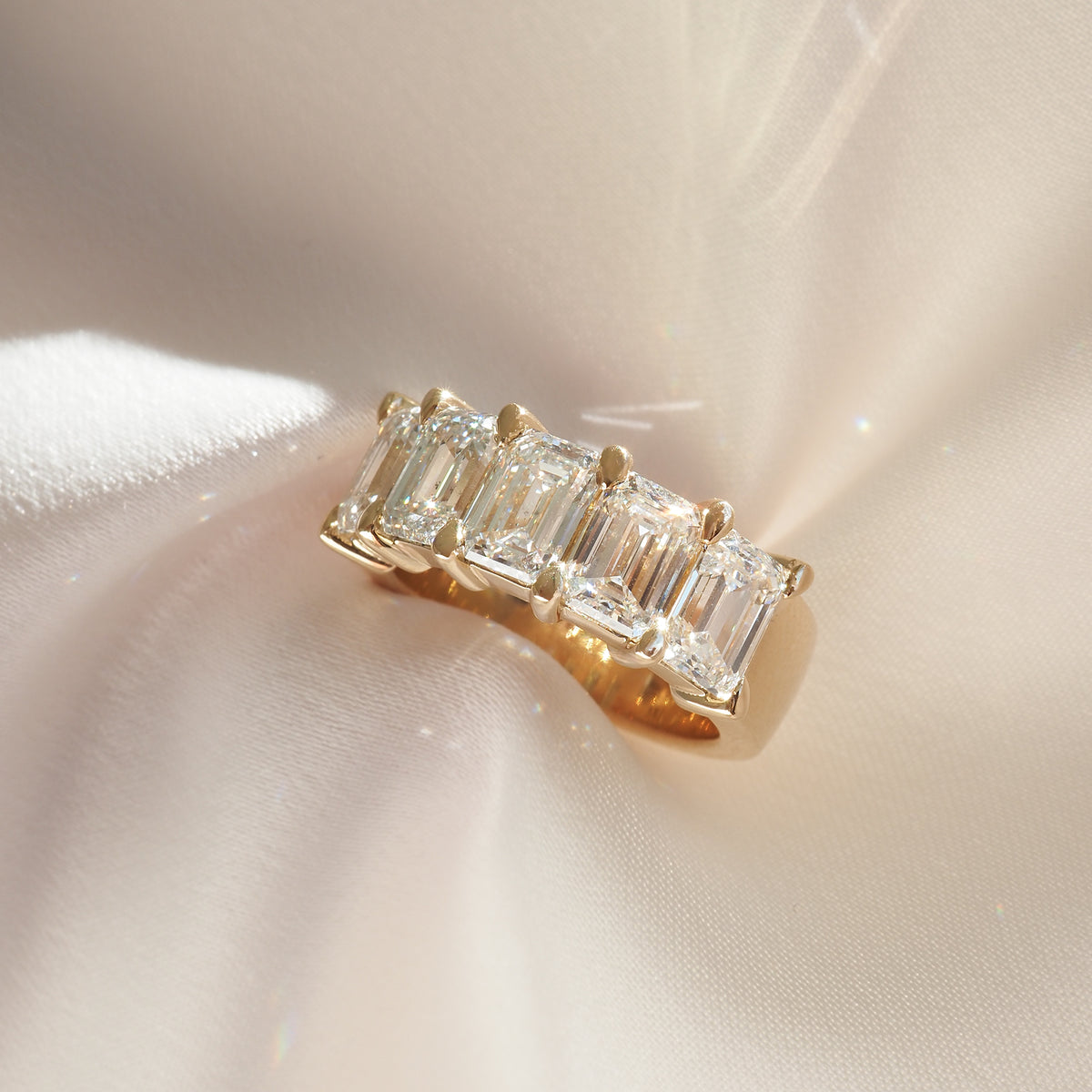 Emerald-cut diamond ring set in gold on a silky fabric, exuding luxury and elegance.