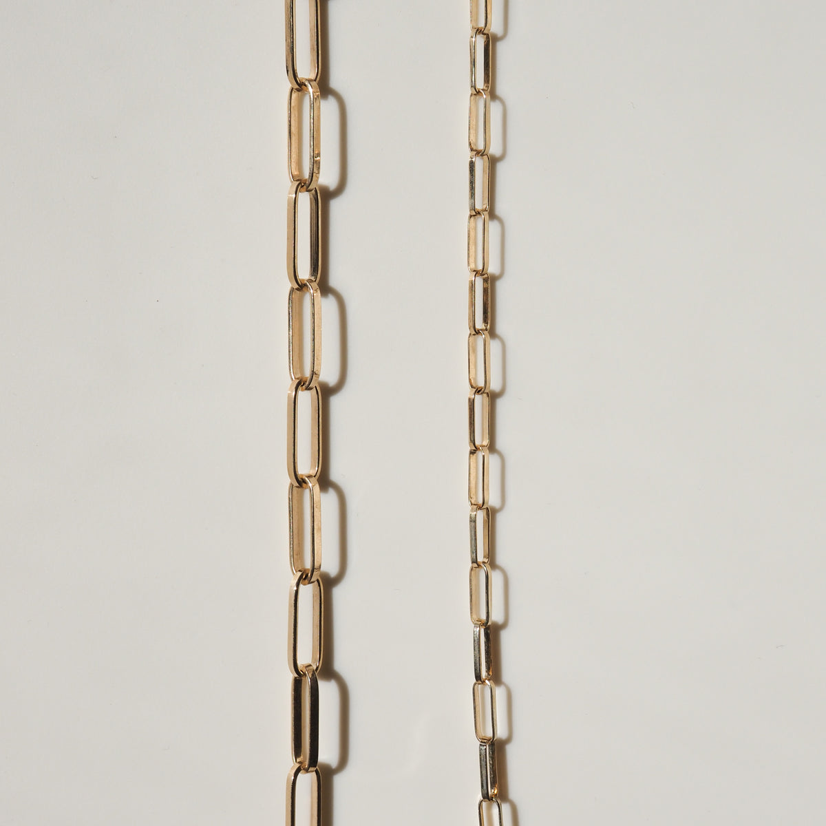 Two elegant gold chain necklaces with elongated rectangular links on a light background, showcasing luxury and high-end jewellery design.