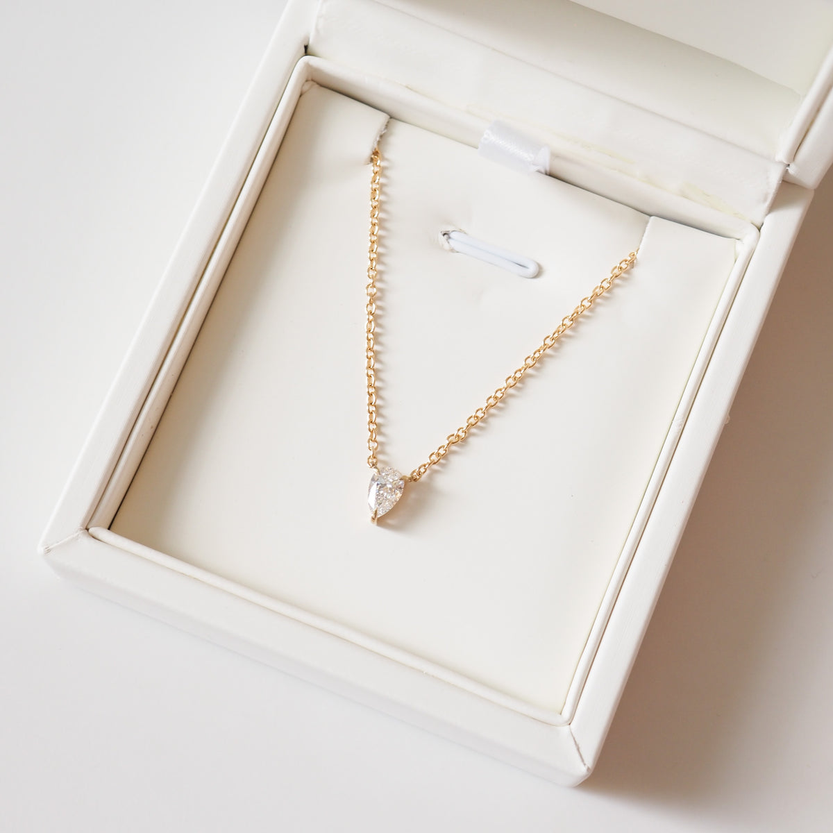 Gold pear-cut diamond necklace displayed in a jewelry box with fixed pendant