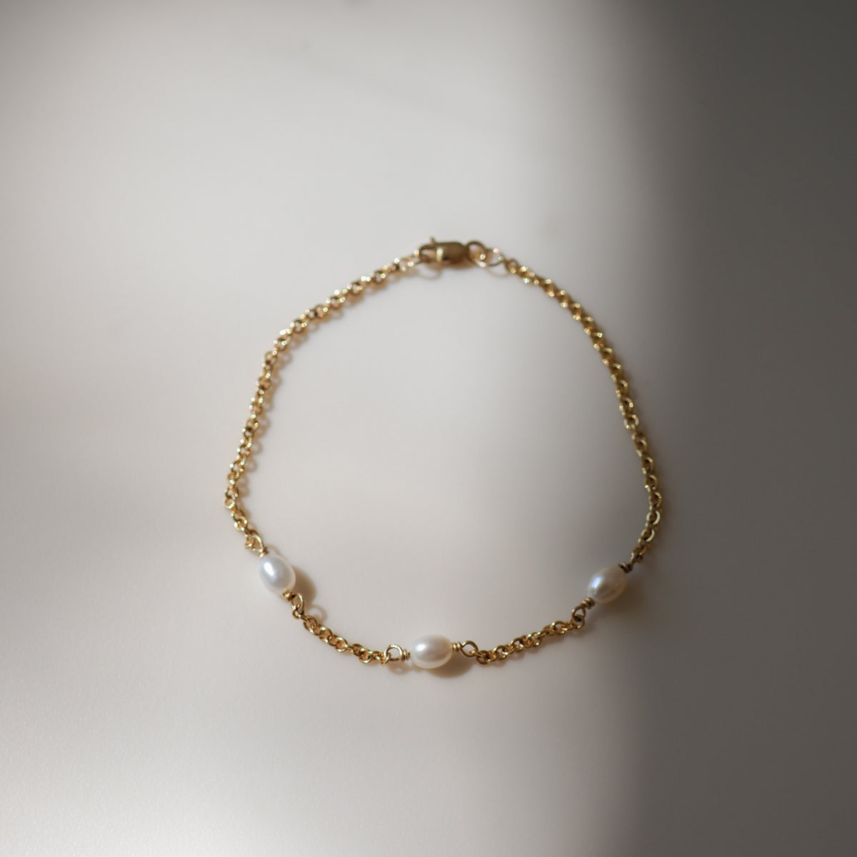 Elegant gold chain bracelet with three freshwater pearls, beautifully laid out on a soft, light surface.