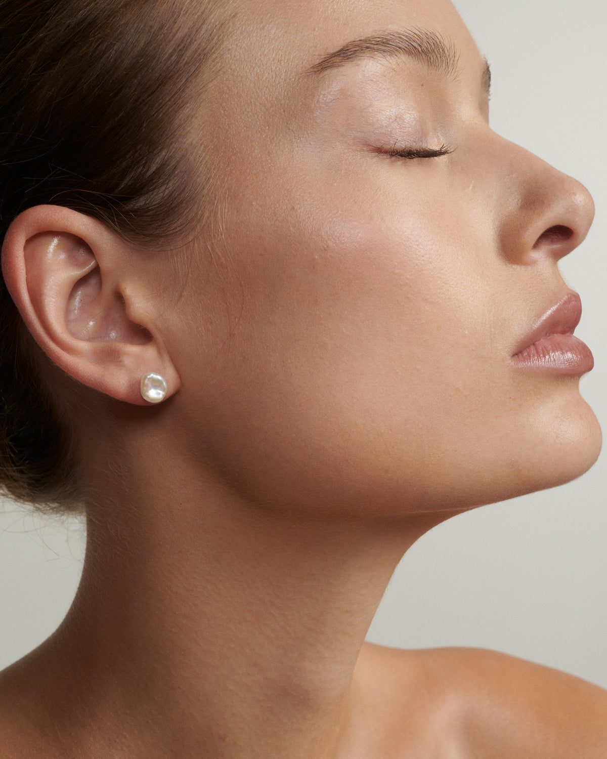 Close-up of a woman's face with a pearl earring on a neutral background