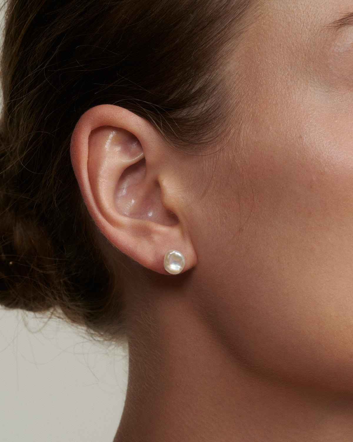 Close-up of an ear wearing a pearl stud earring with a neutral background