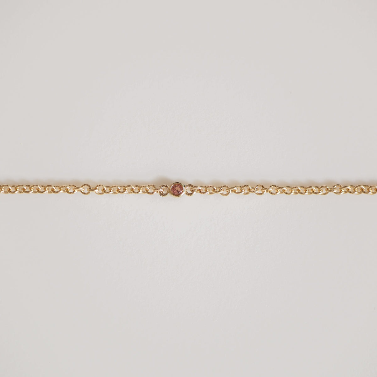 Gold chain with a single, small pink diamond in the centre. Elegant and minimalist luxury jewellery on a plain white background.