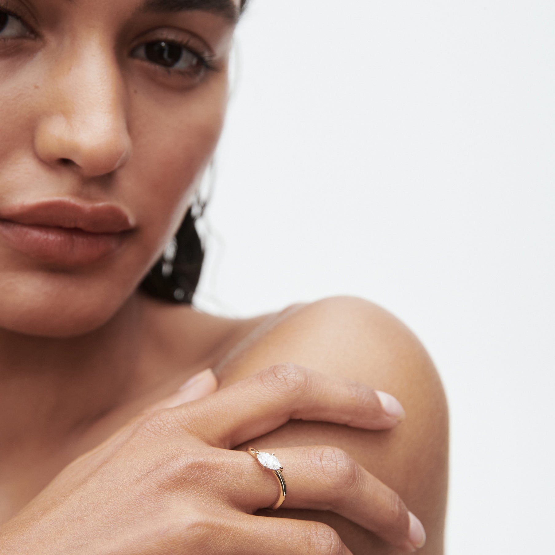 Woman wearing a gold ring with a pear-shaped diamond, close-up on her hand and part of her face with neutral expression.