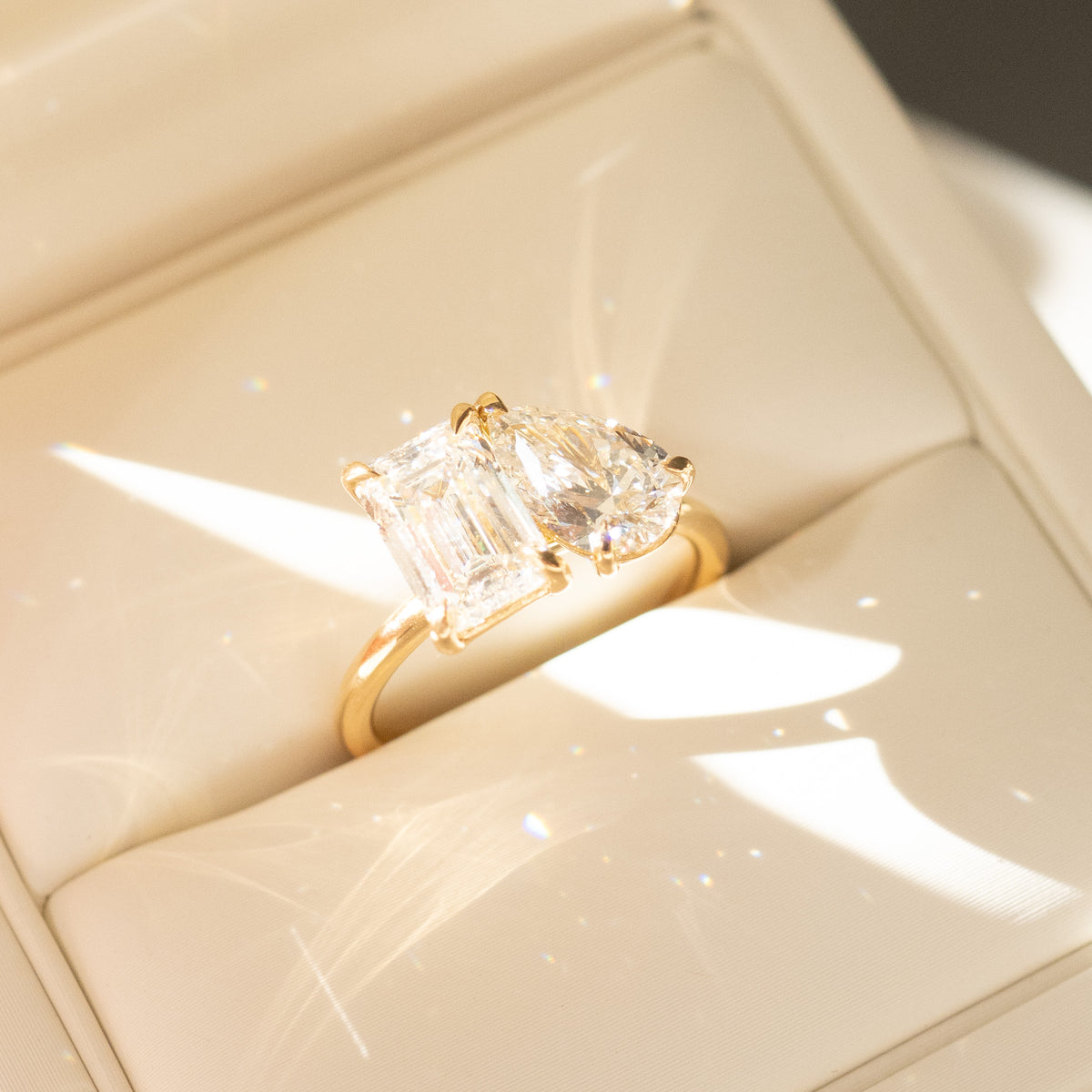 Yellow gold engagement ring with emerald-cut center and pear-shaped side diamond