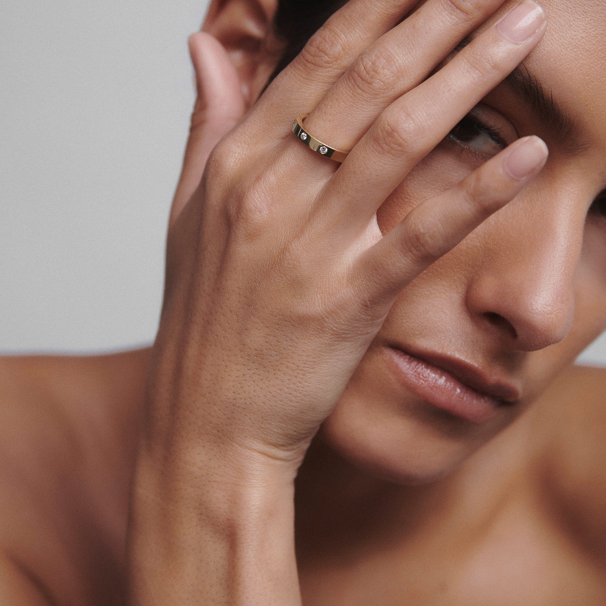 Close-up of a person's hand touching face, wearing a sleek gold ring with embedded diamonds, evoking luxury jewellery and elegance.