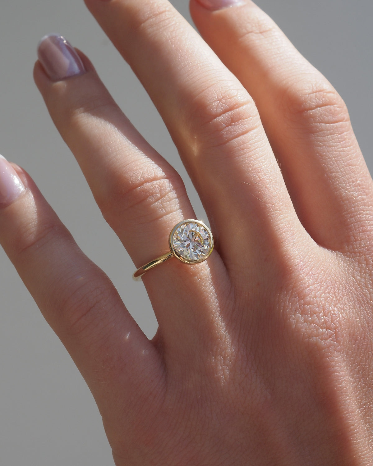 Gold round bezel solitaire diamond ring on hand, thin band
