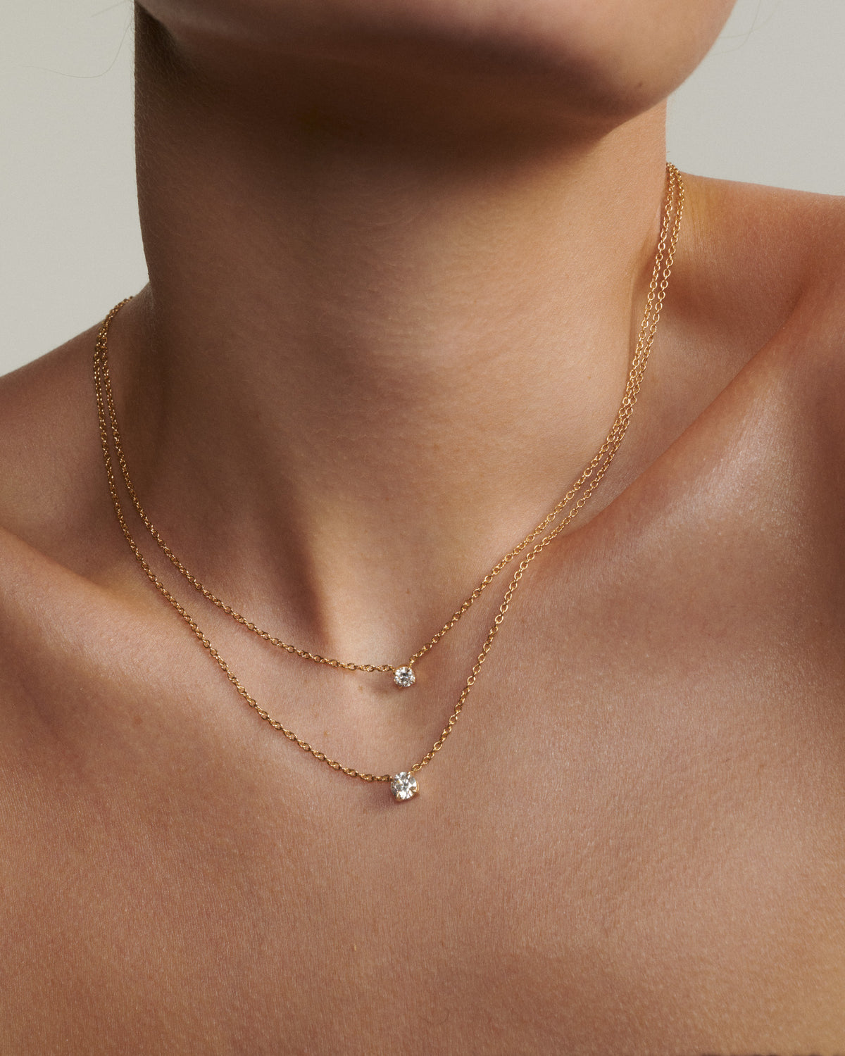 Gold necklace with small pendants on a person's neck against a neutral background