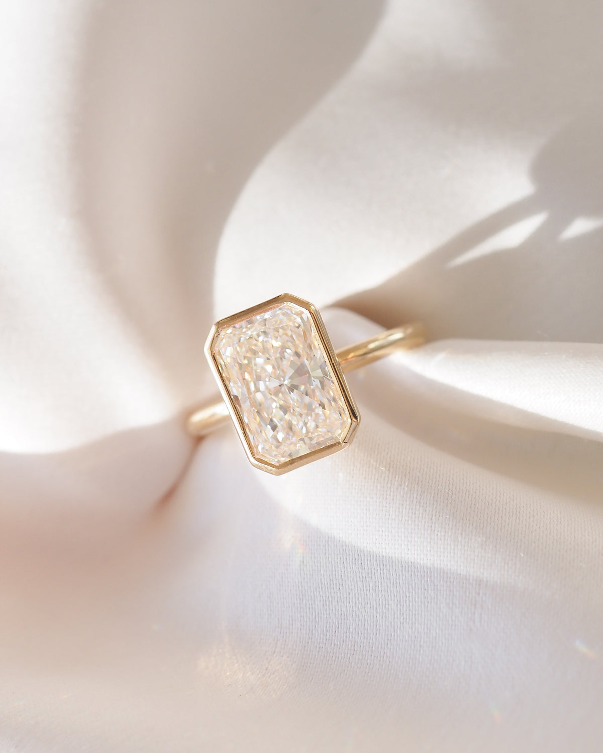 Gold band ring with square bezel-set radiant-cut diamond, close-up view