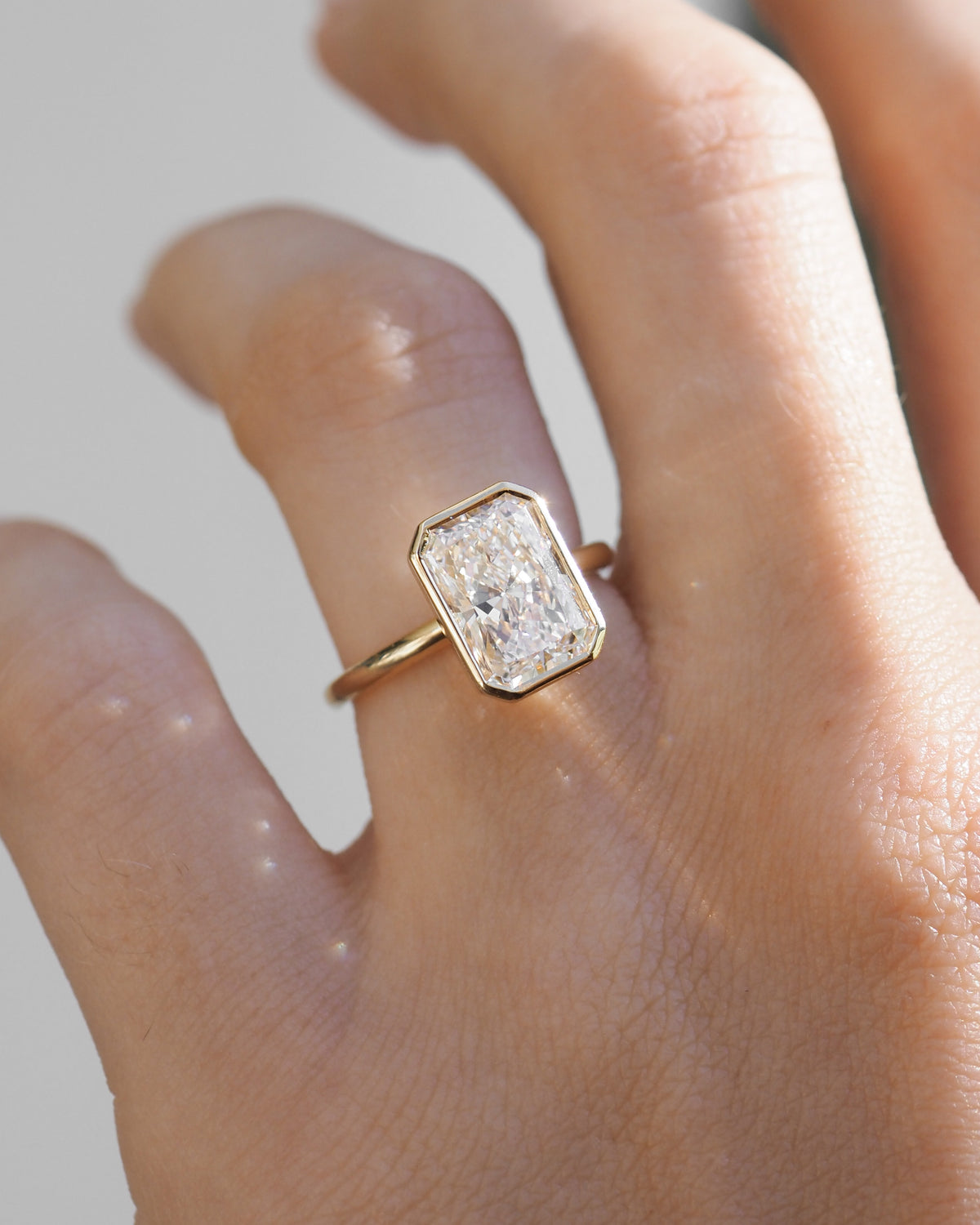 Gold band ring with square bezel-set radiant-cut diamond worn on hand