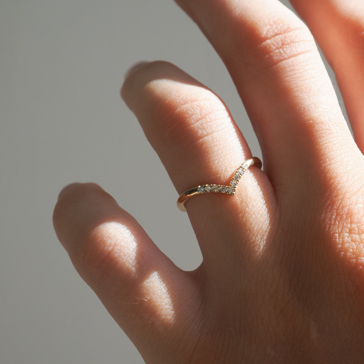 Hand wearing a delicate gold ring with a row of small diamonds in a V-shape, capturing soft natural light.