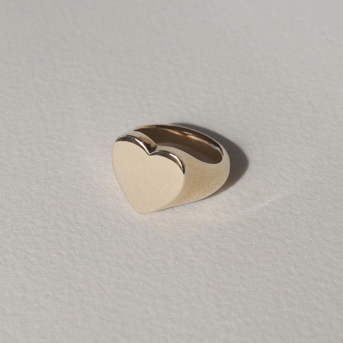 Gold heart-shaped ring on a light textured background, showcasing minimalist luxury jewellery design.
