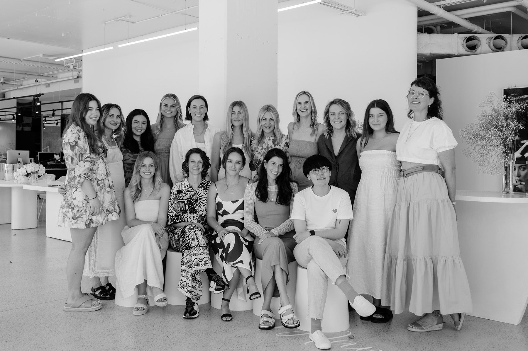A group of 17 fashionable women pose indoors, showcasing diverse patterns and styles, reflecting elegance in a modern jewellery design studio setting.