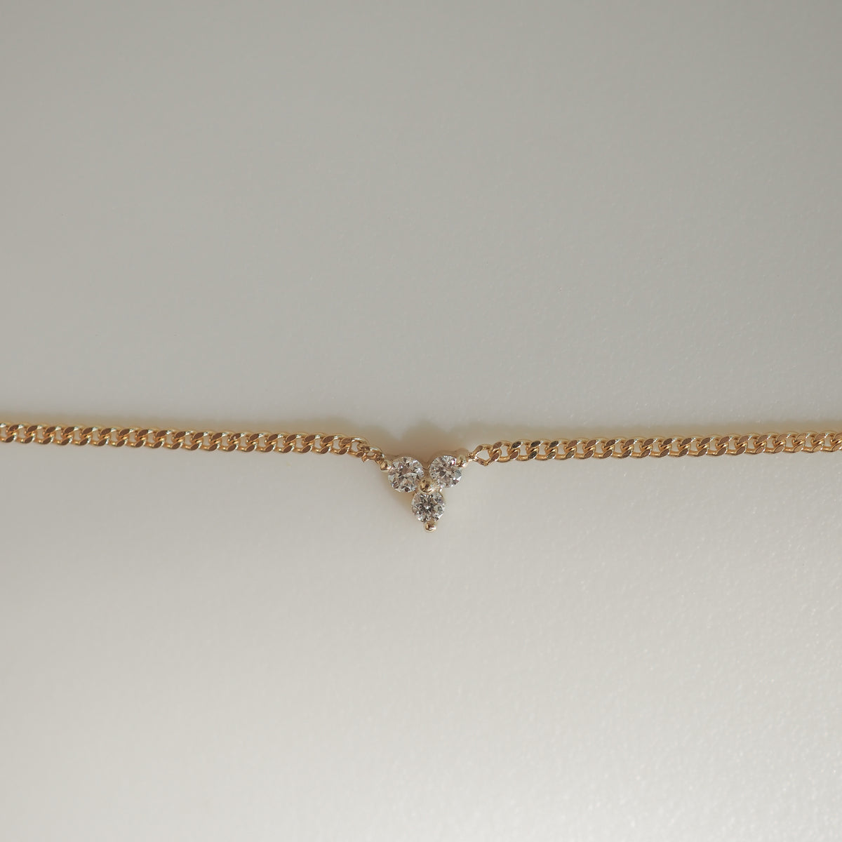 Gold chain necklace with a V-shaped cluster of sparkling diamonds at the centre, set against a soft, light background.