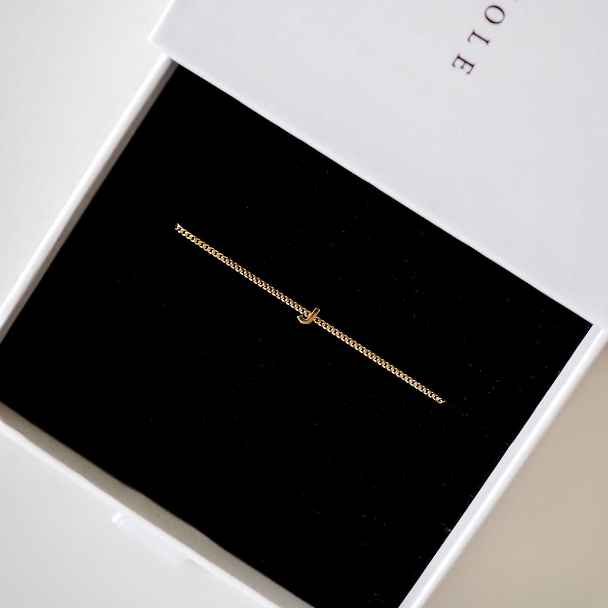 Gold chain bracelet with a small elegant charm displayed in a luxurious black and white jewellery box.