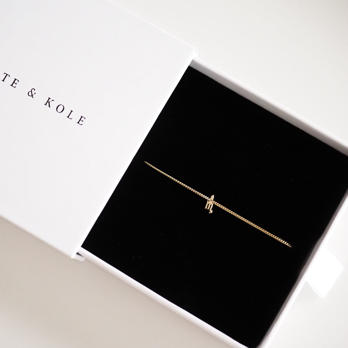 Delicate gold bracelet with a tiny charm in a sleek black jewellery box, partially covered by a white lid.
[text overlay: Scorpio] [text colour: #000000]
