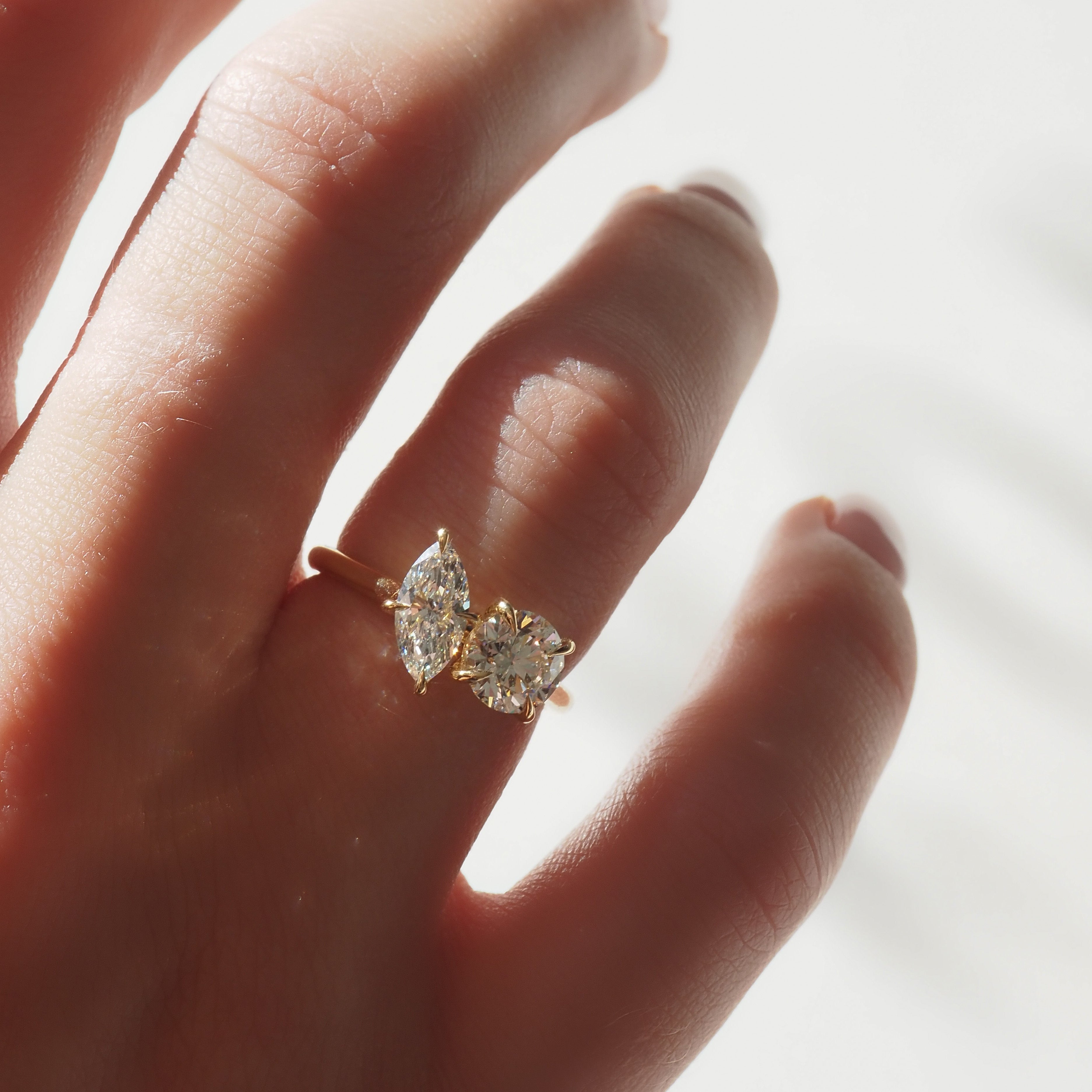 Elegant gold ring with two sparkling, marquise-cut diamonds showcased on a left hand. Luxury jewellery, minimalist design.