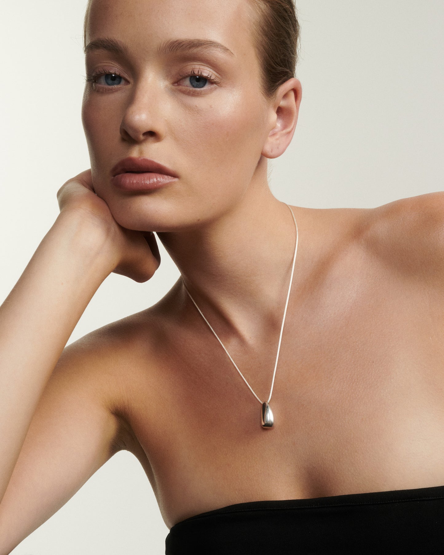 Woman wearing a silver necklace against a plain background