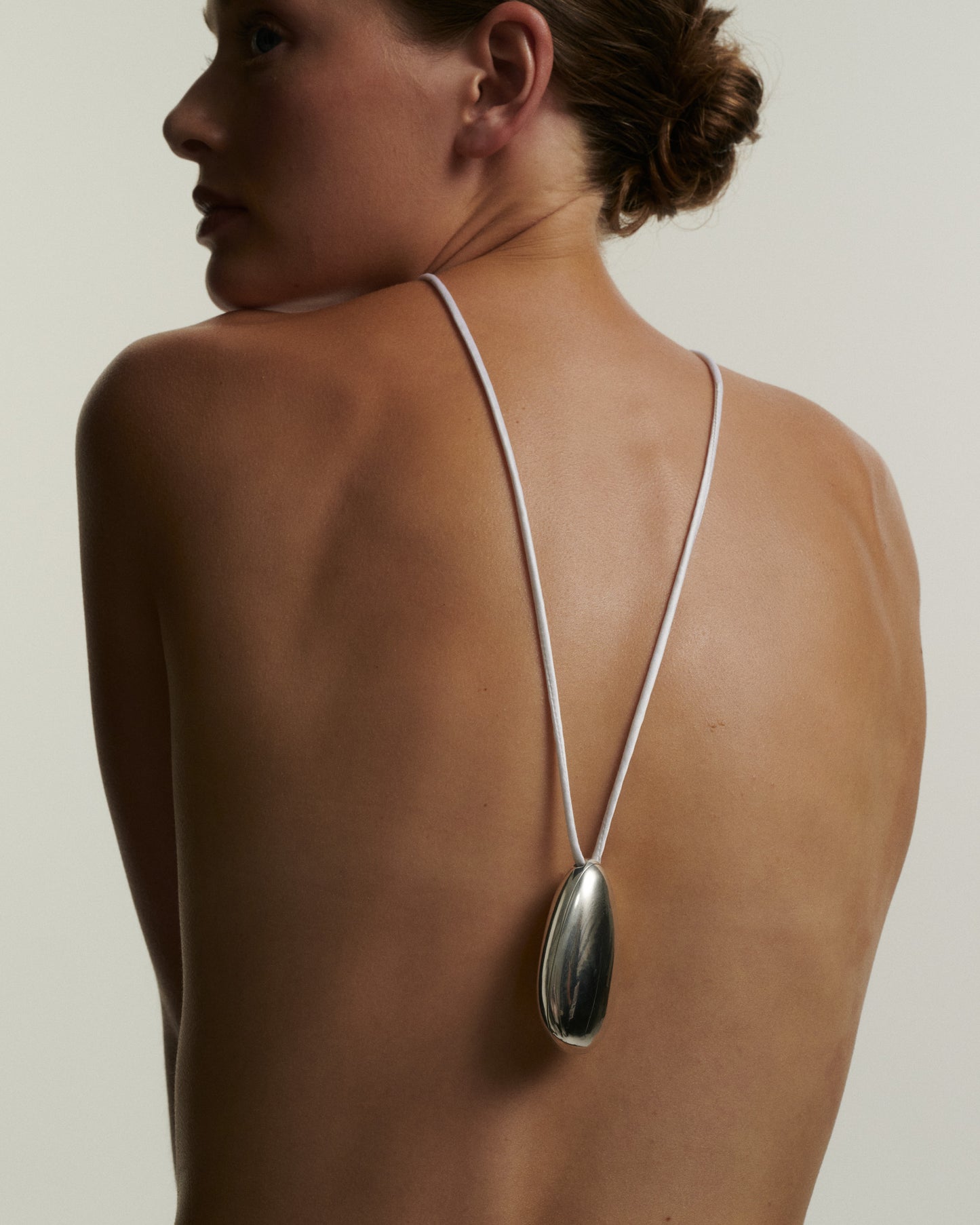 Woman wearing a silver necklace with a large pendant on a plain background