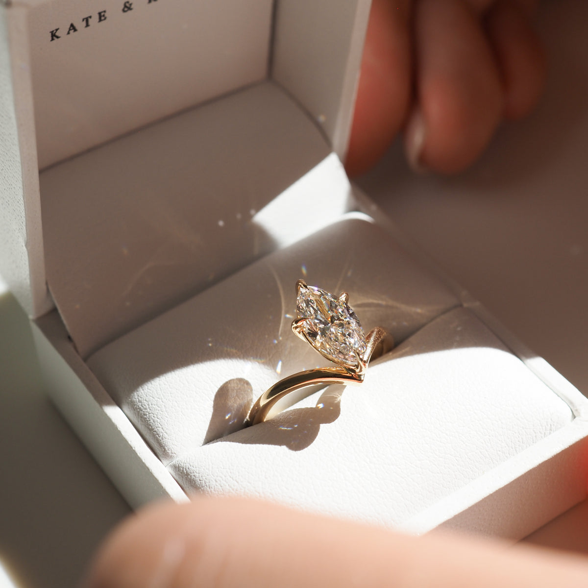 A marquise-cut diamond ring in a gold setting nestled in a white jewellery box, delicately showcased under soft lighting, ideal for luxury gifting.