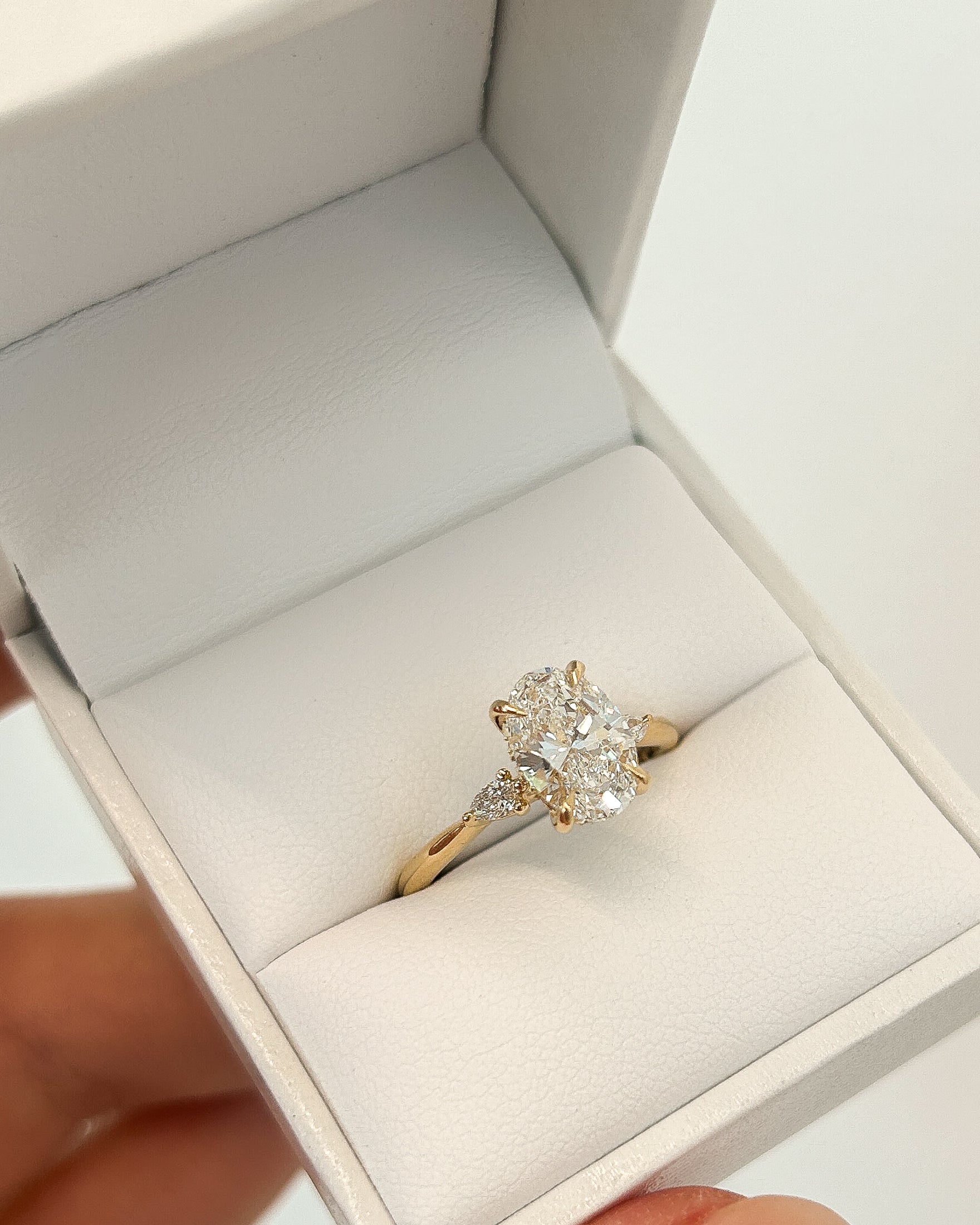 Gold ring with a large oval diamond and side stones in an open jewellery box. Luxurious and elegant design.