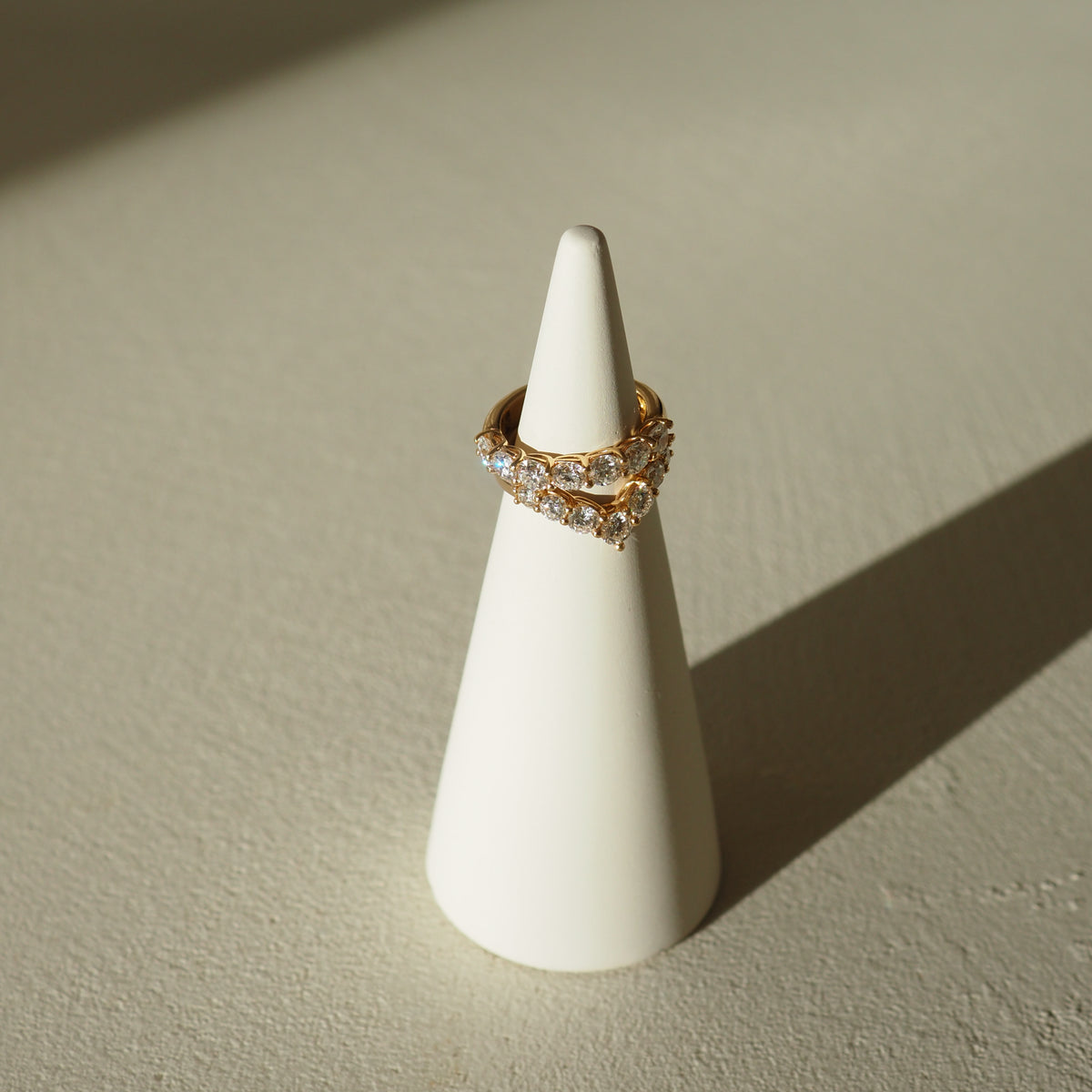 Gold ring with gemstones on a white cone-shaped stand against a beige background