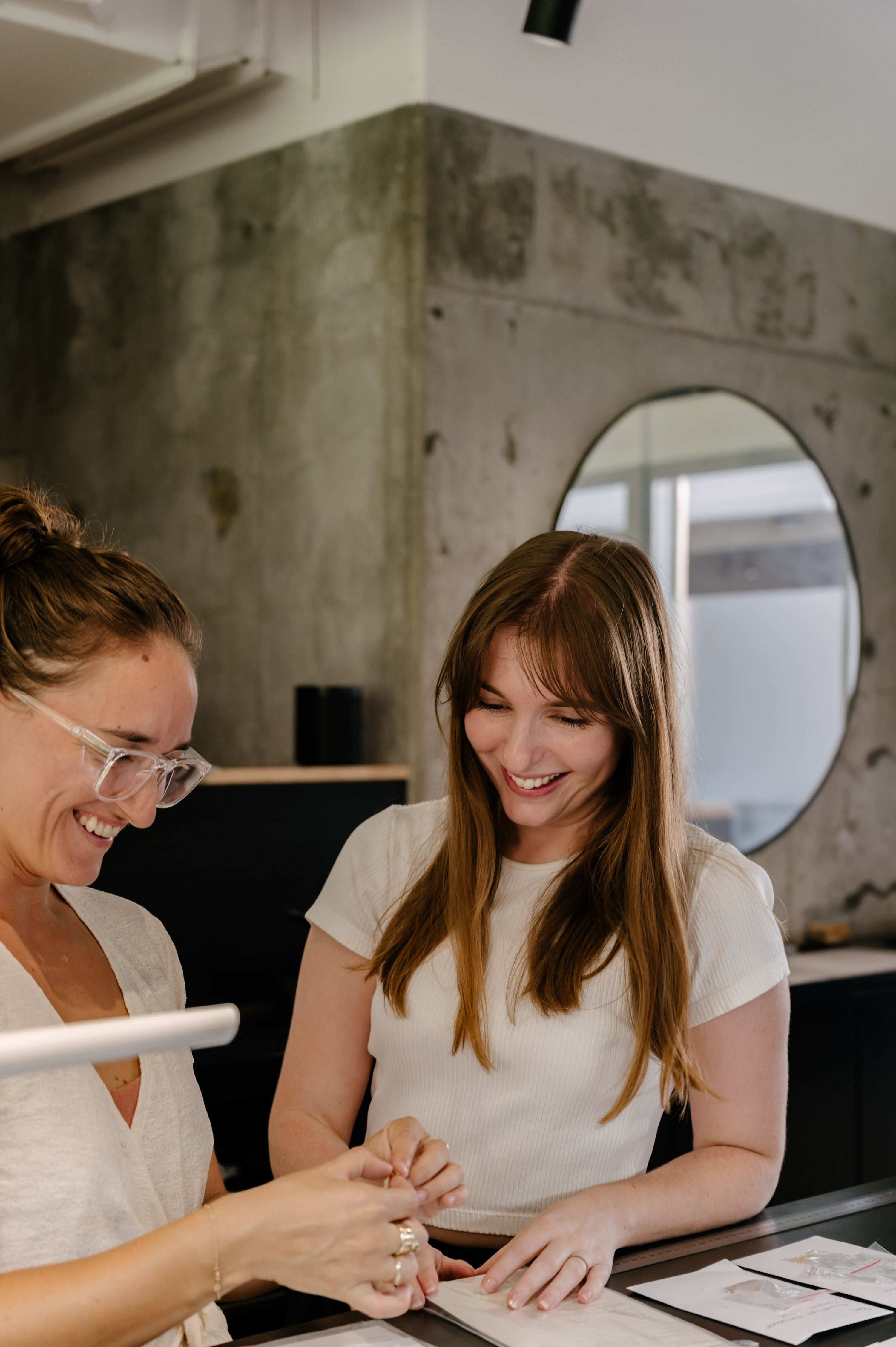 Two women smiling and examining jewellery pieces in a luxury store with a modern and minimalist interior design.