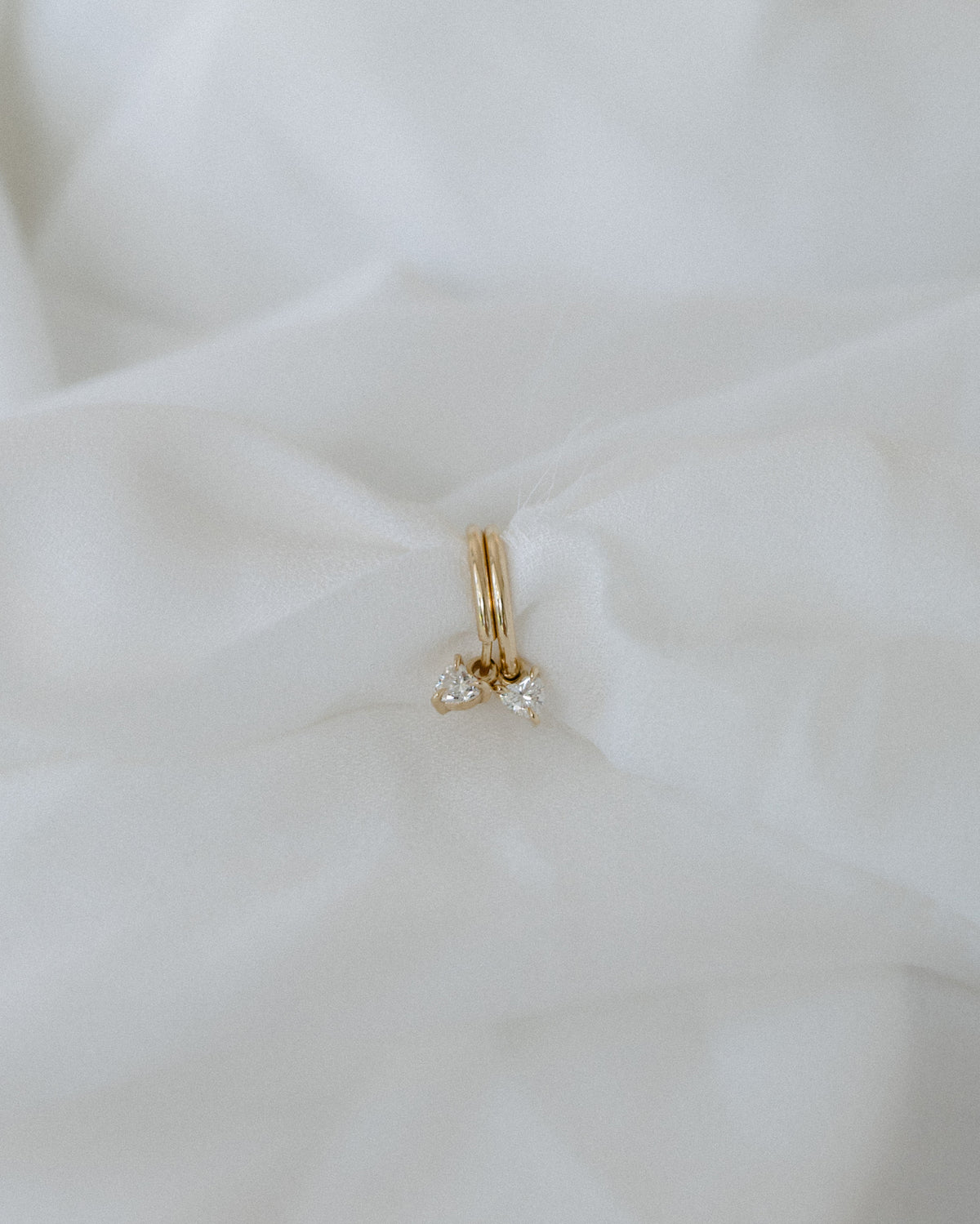 Gold earrings with diamond pendants on soft white fabric, showcasing luxury jewellery design. Elegant and high-end accessory style.