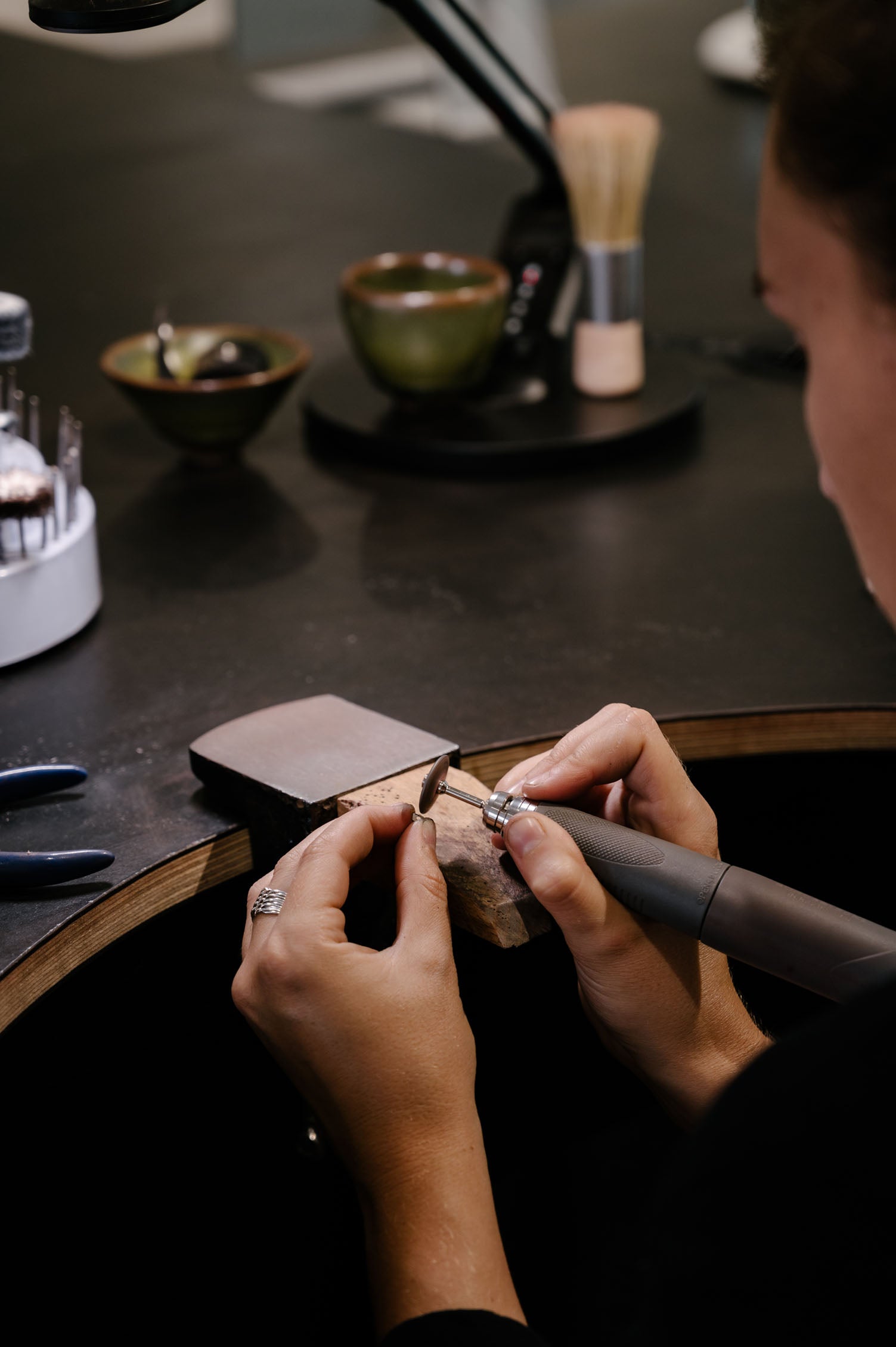 Hands crafting a luxury ring at a jewellery bench, surrounded by tools and materials, highlighting artisanal craftsmanship in fine jewellery.
