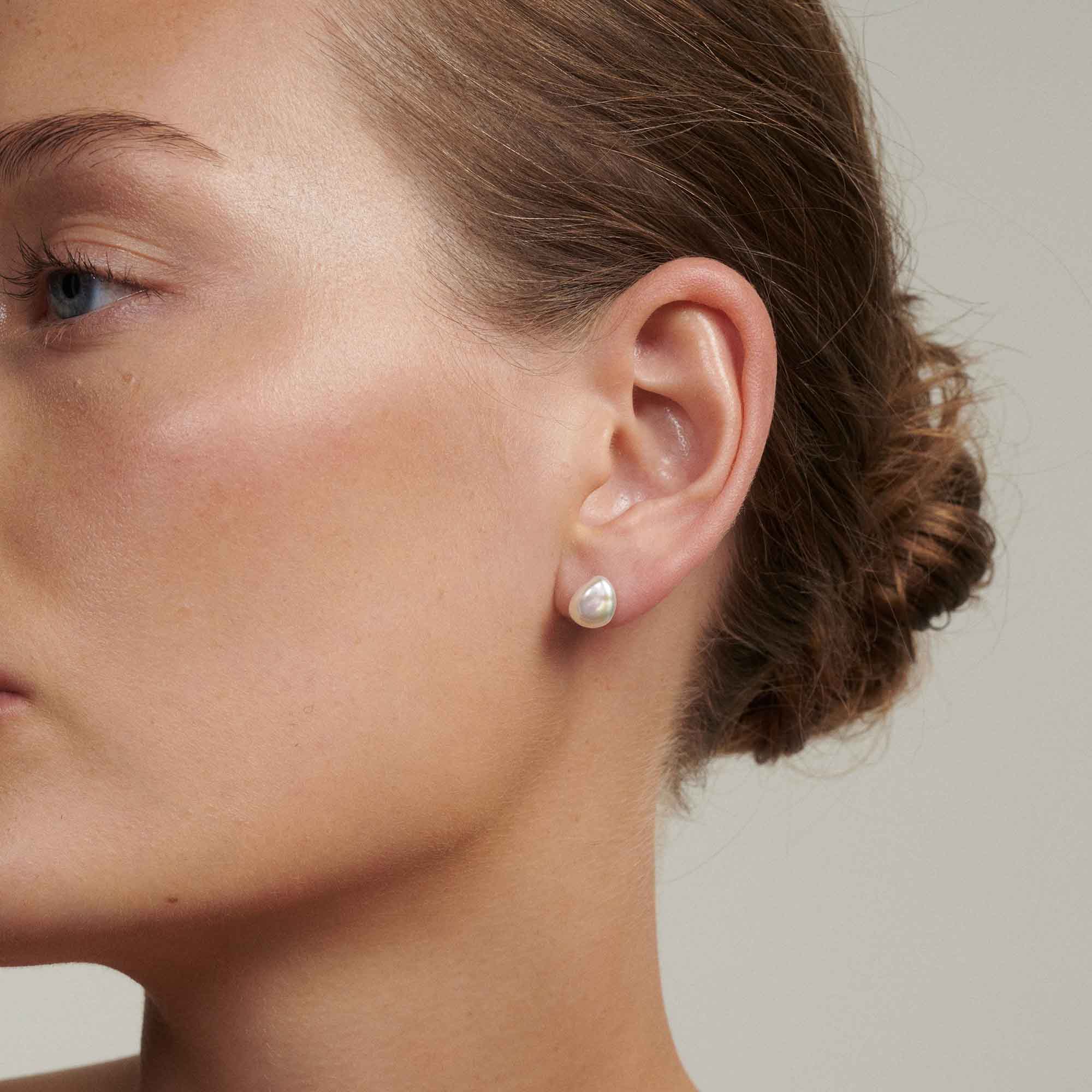 Close-up of a person wearing pearl earrings with a neutral background